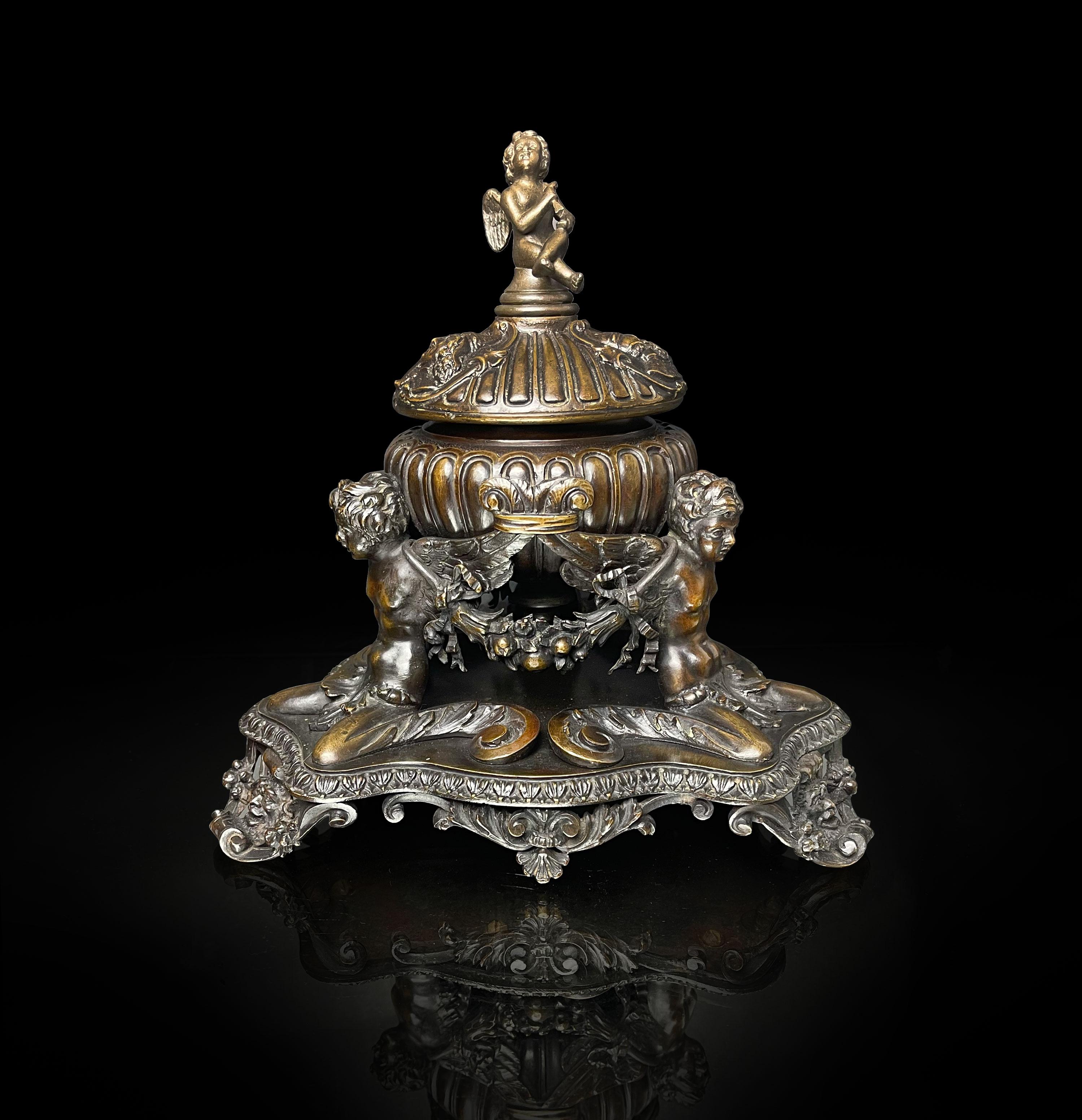 An Elaborated Renaissance style patinated bronze inkwell by e.f. Caldwell & Co., New York, Early 20th Century. surmounted by a putti and supported by three winged cherubs joined by flower garlands.
Measures: Height: 10 in. (25.4 cm)
Width: 7.75