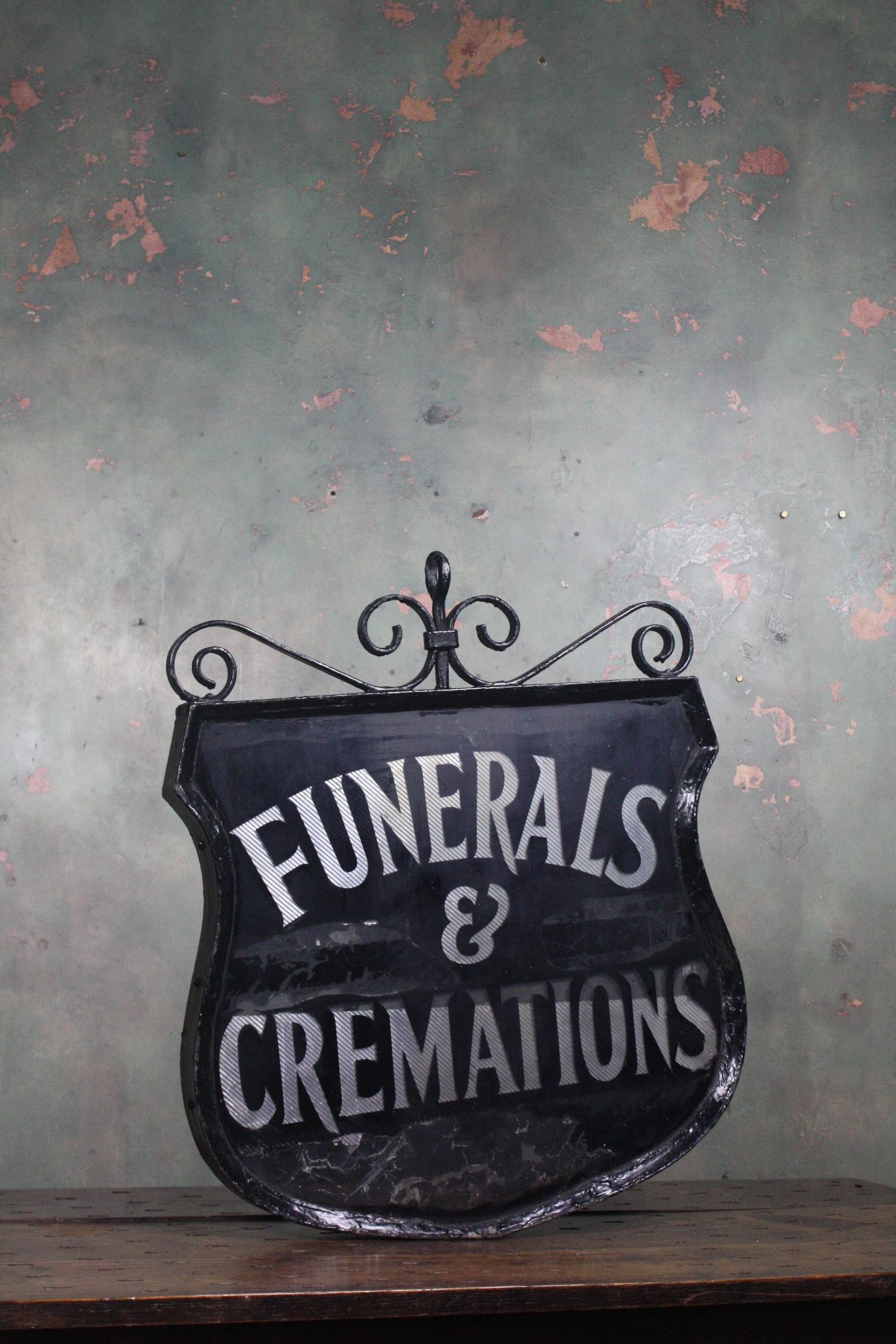 Here we have a large reverse painted early 20th century in age, doubled sided trade sign from a funeral directors. Encased in a iron frame, with scroll work and a single hanging hook. Reverse painted glass front and back with a reflective interior.