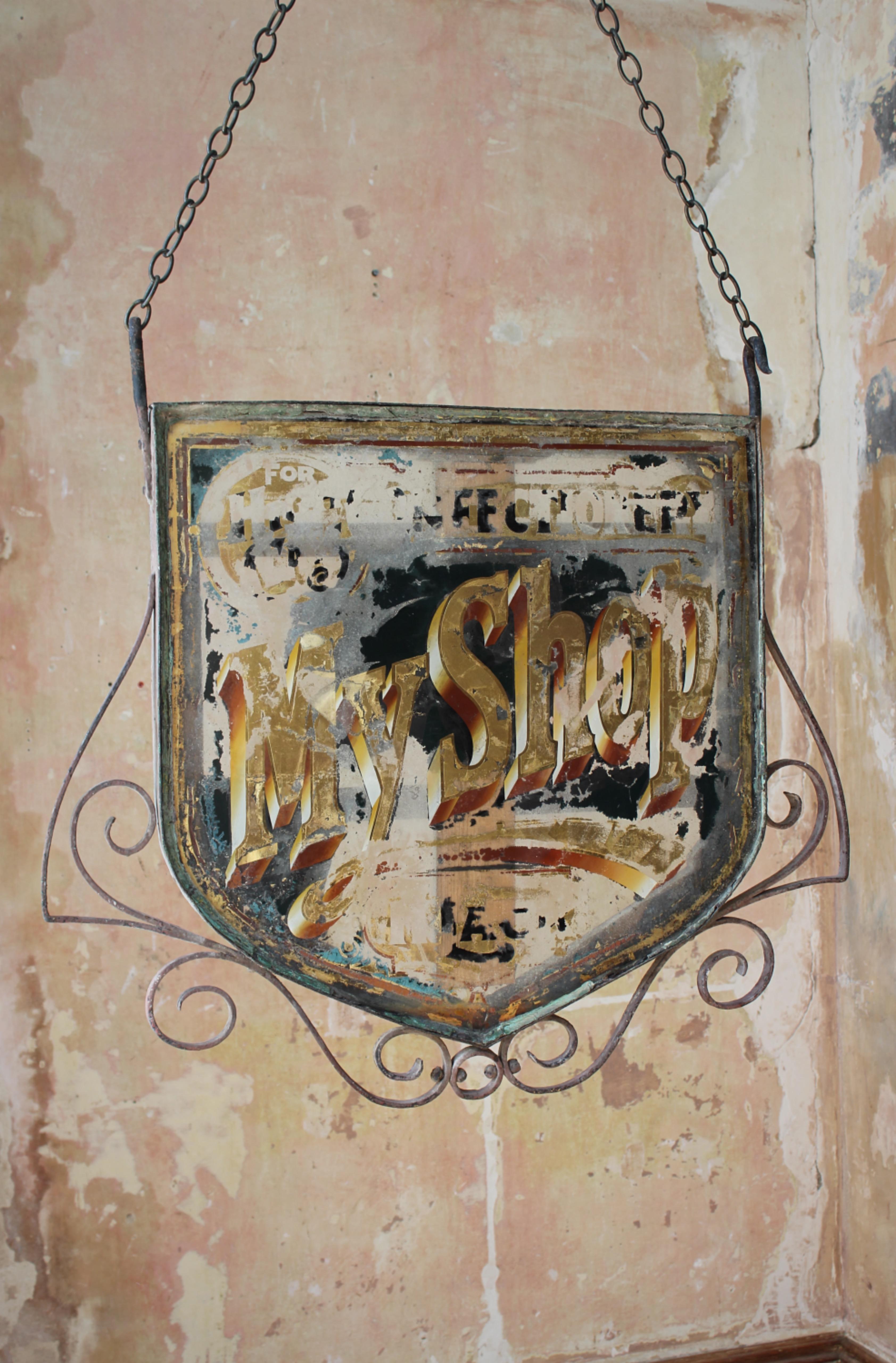 A large reverse painted hanging trade sign, wrought iron frame with internal wooden supports.

The reverse painted glass has losses, it appears the sign would of read 
