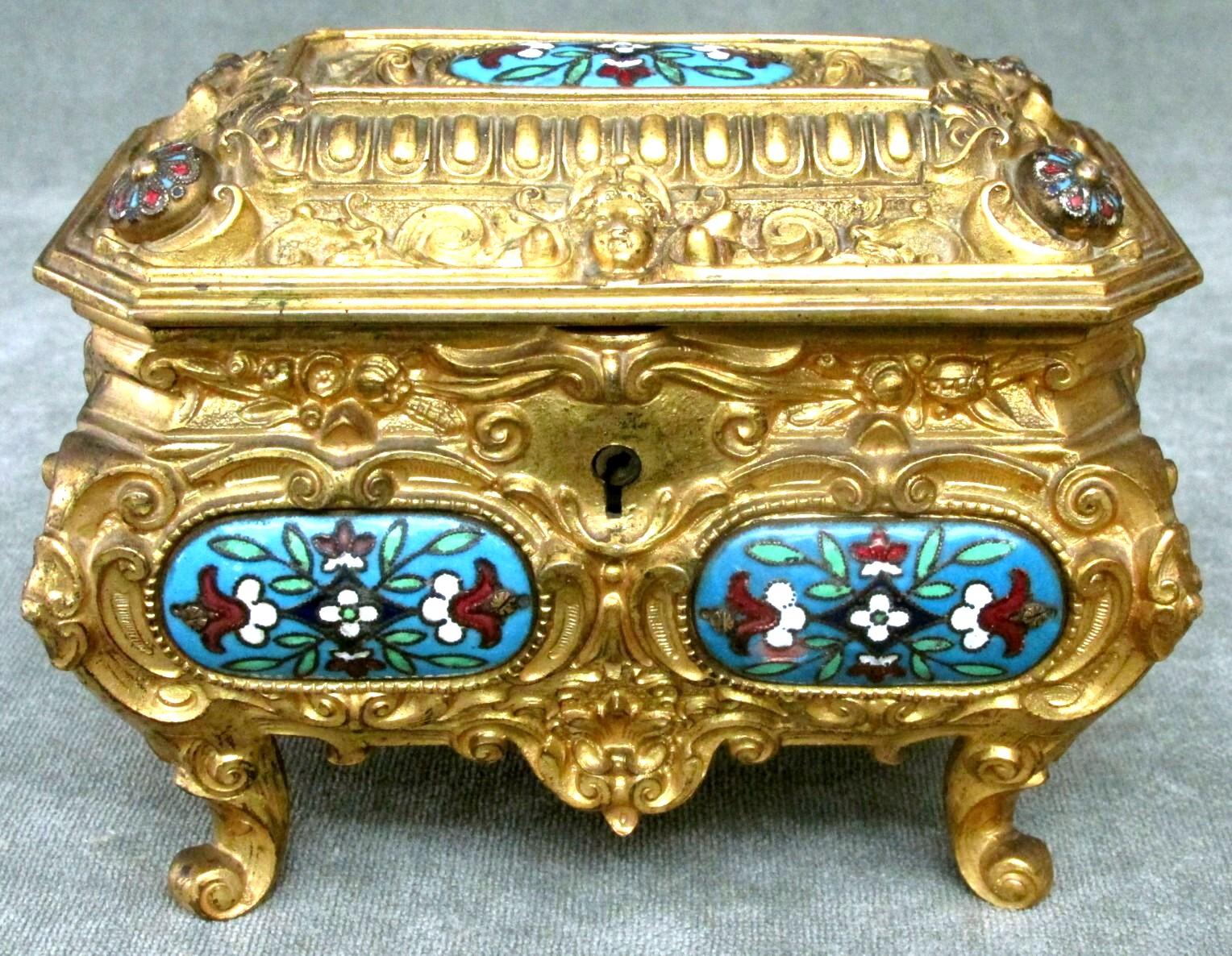 The richly gilded bombe-shaped body decorated overall with foliate and scrolled elements, the front, sides and hinged top inset with turquoise enamel panels decorated with floral geometric motifs, the lid opening to a velvet lined interior, raised