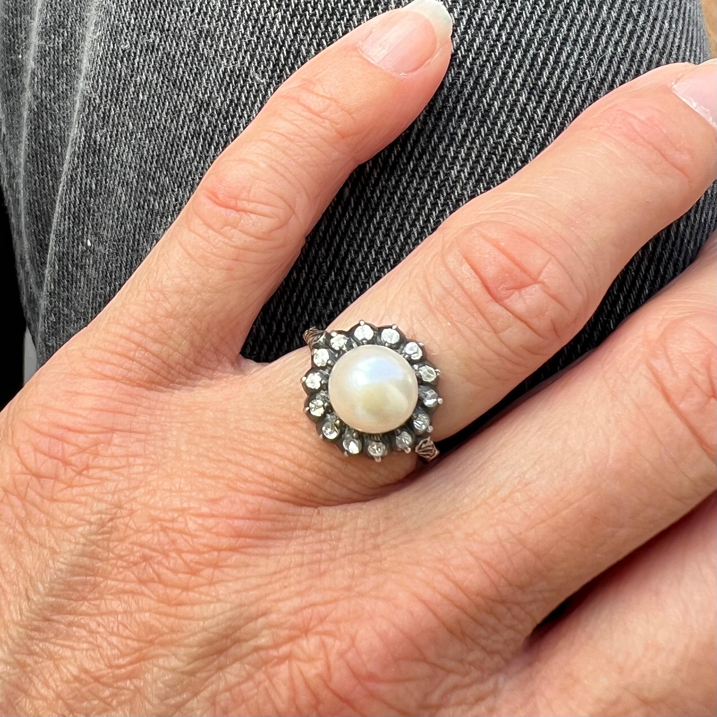 Este precioso anillo tiene como pieza central una luminosa perla cultivada, que mide aproximadamente 14 mm de diámetro. La perla está rodeada por un halo de brillantes diamantes talla rosa, engastados individualmente en plata, que crean un delicado