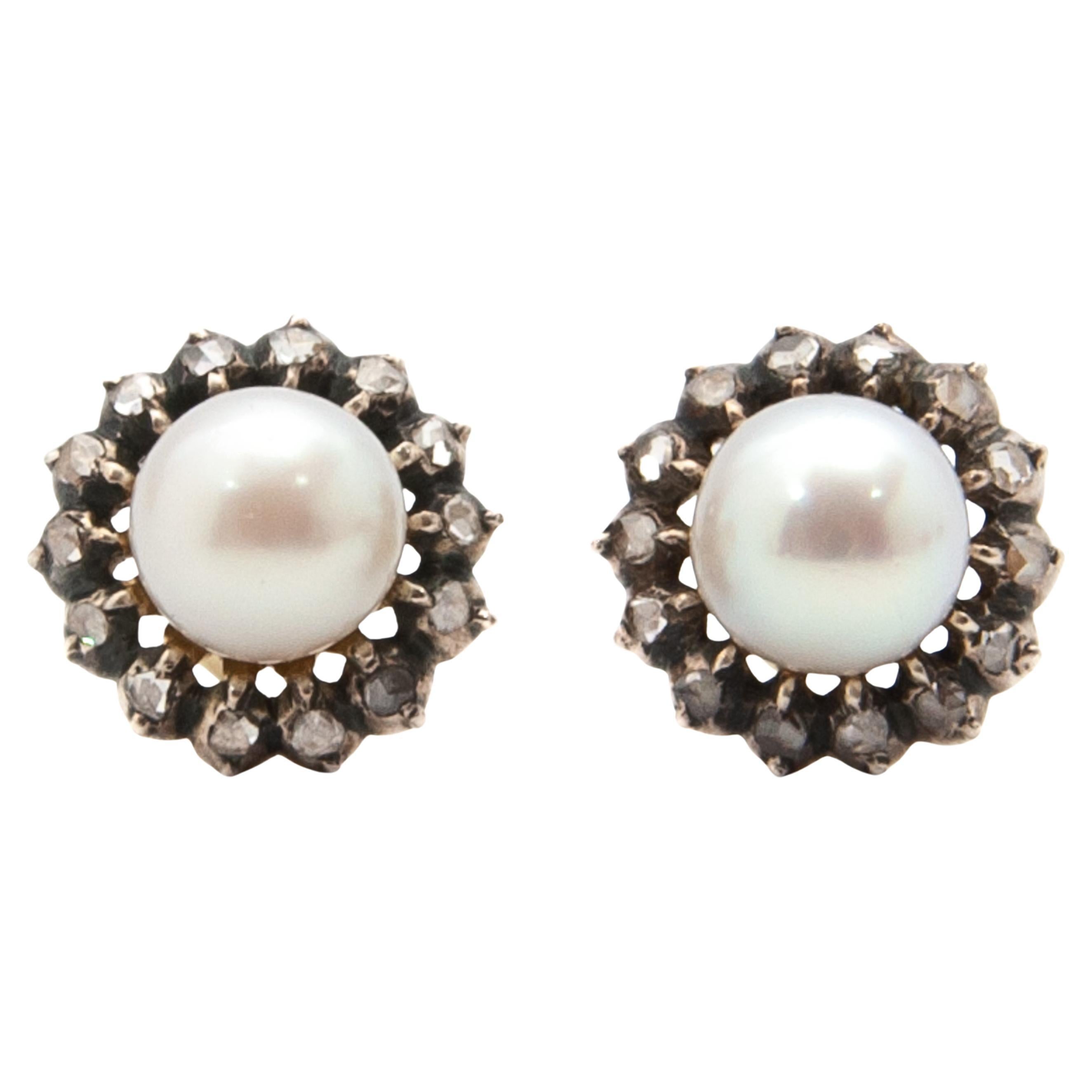 Estos elegantes pendientes presentan luminosas perlas cultivadas blancas de aproximadamente 14 milímetros de diámetro, cada una enmarcada por un halo de diamantes talla rosa de estilo antiguo. Los diamantes están engastados en plata y oro amarillo