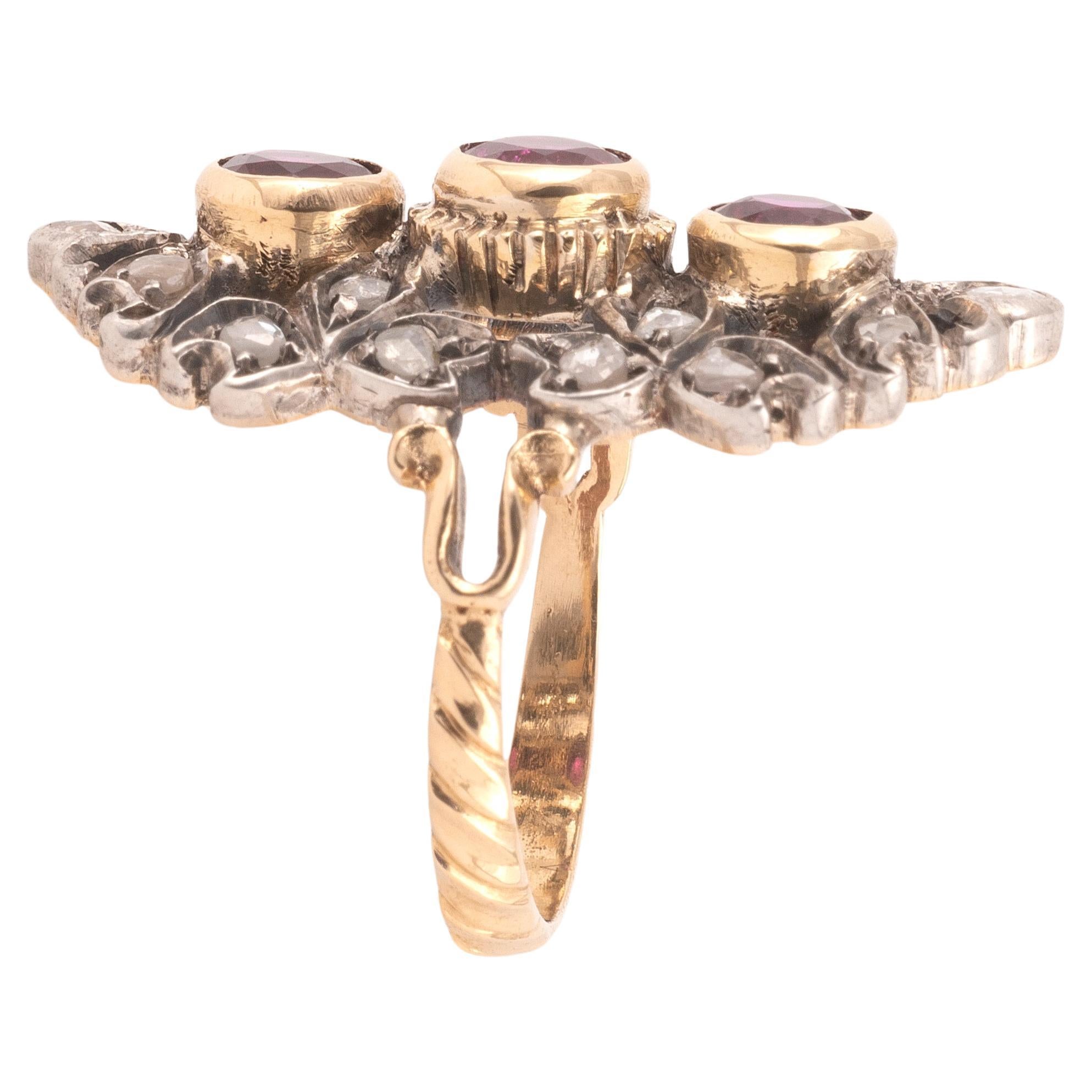 I tre rubini ovali incastonati in formazione verticale, all'interno di un bordo di diamanti tagliati a rosa, montati in argento e oro.
Dimensioni: 61/2
Peso: 7 grammi.


