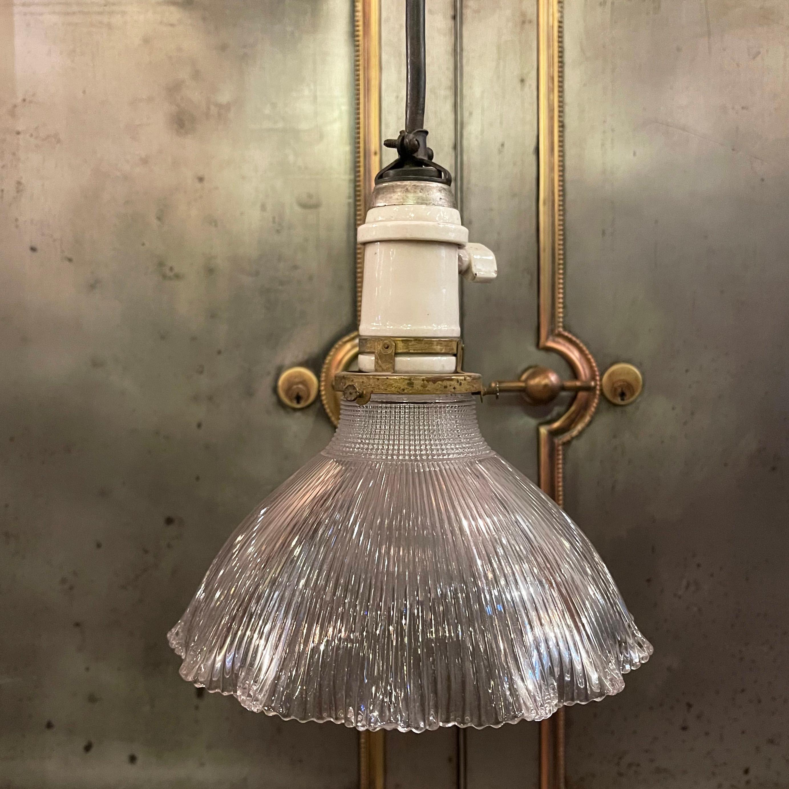 Early 20th century, industrial pendant light with ruffle edged, prismatic Holophane glass dome shade, brass fitter, porcelain socket and canopy on metal backplate hangs at an overall height of 20 inches. 