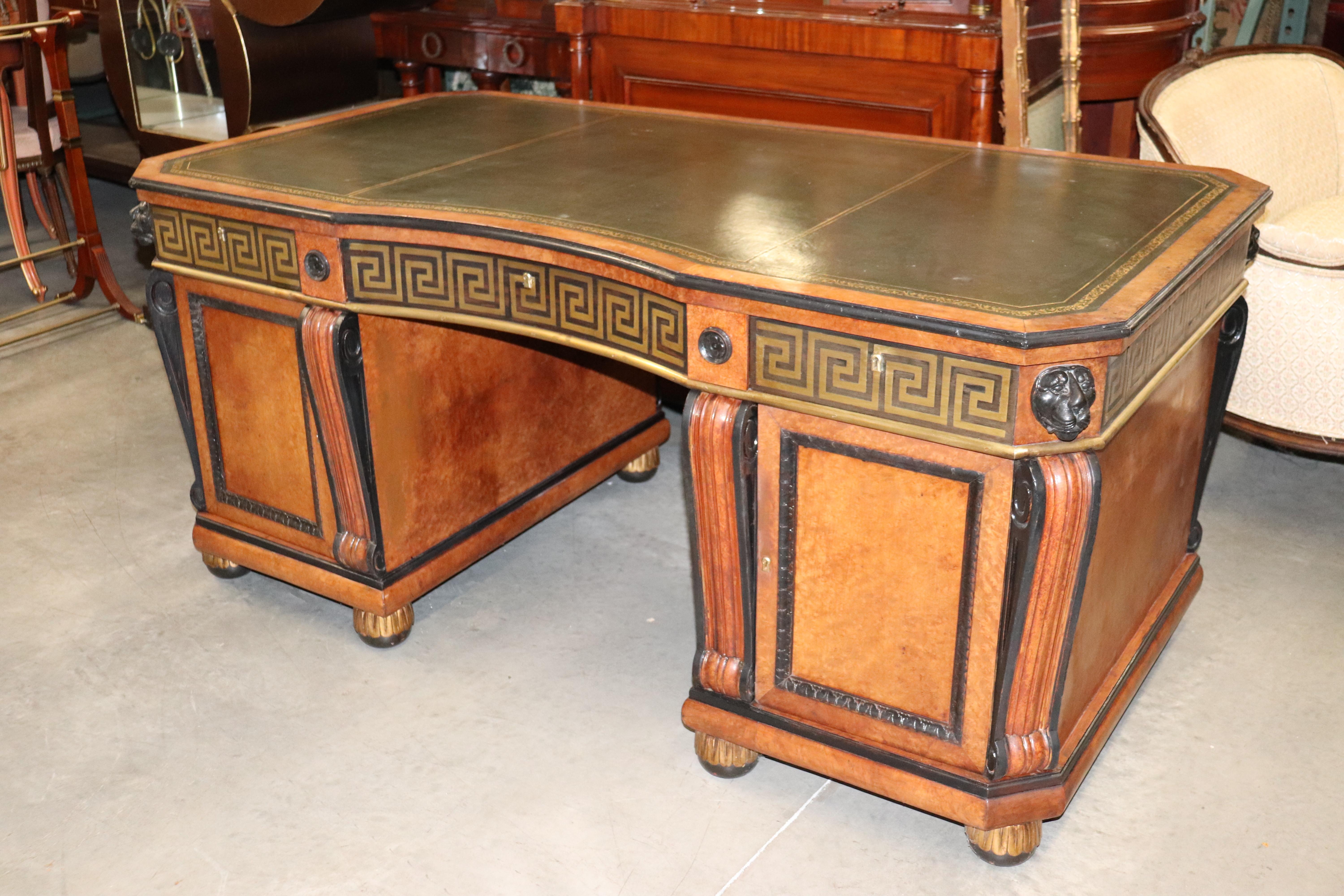 This is a gorgeous brass inlaid desk with Greek key motif. The desk is made of burled walnut and features lion heads on each corner. The desk measures 31 tall x 67 wide x 37 deep.
