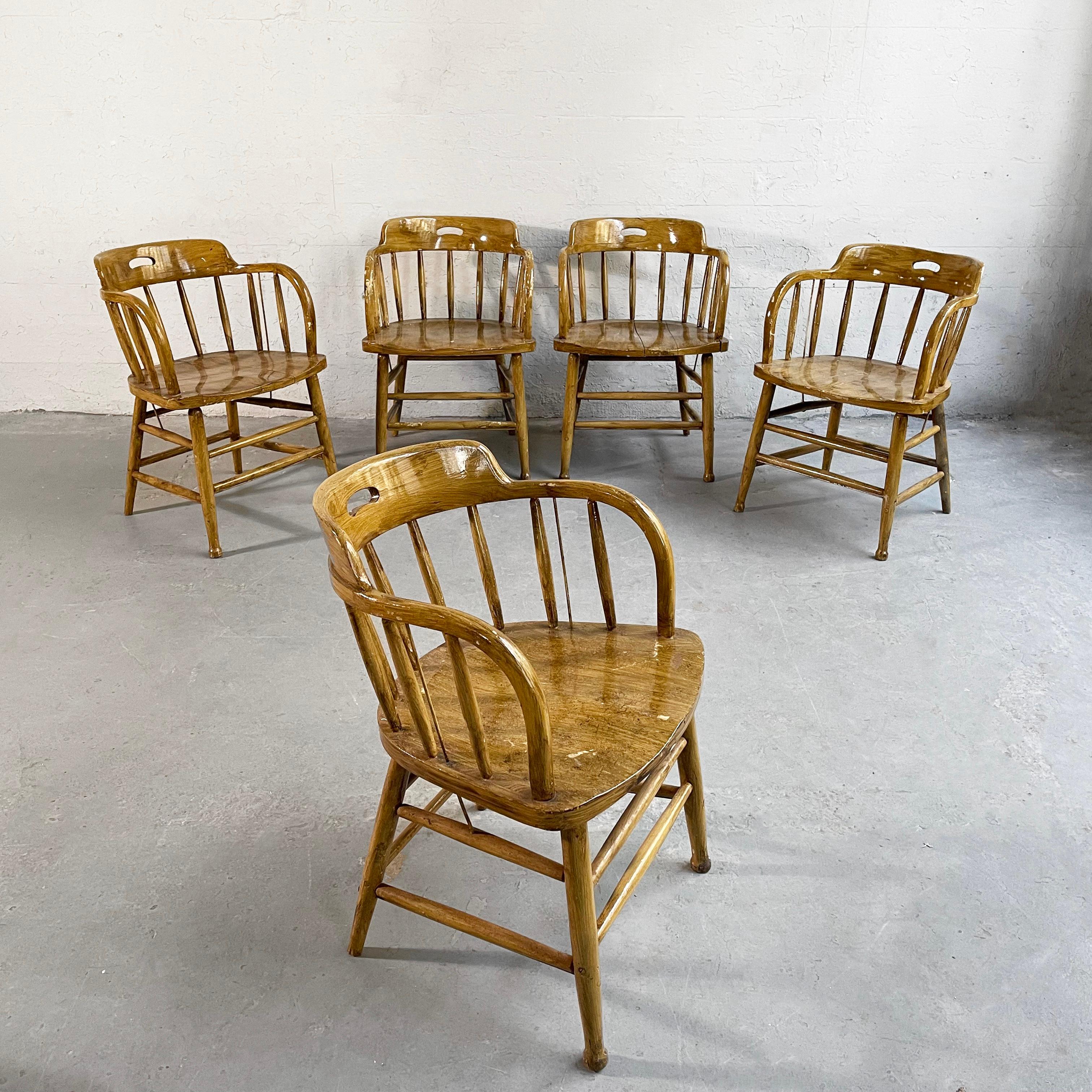 Set of five, classic, early 20th century, craftsman, lacquered oak, firehouse dining armchairs feature spindle backs and sides with metal reinforcement rods. The chairs retain their wonderful, original patina. A contrasting captain's chair can be