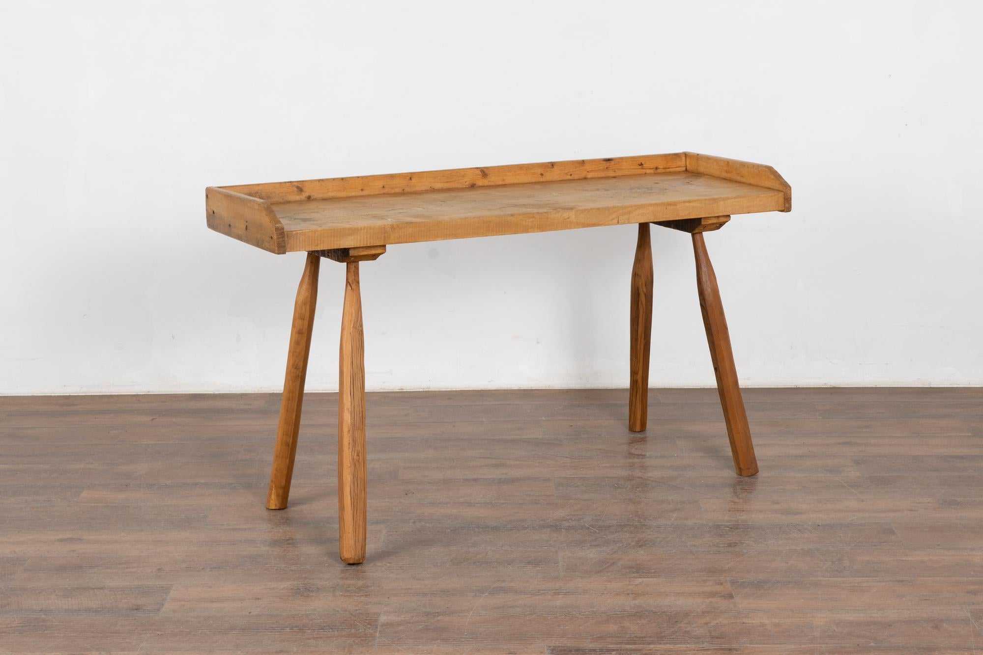 This rustic plank top console table with splay peg legs originally served as a work table. Note the trim/edge around three sides.
The top reveals generations of use in the heavy gouges, cracks, and stains which add character and intrigue to the