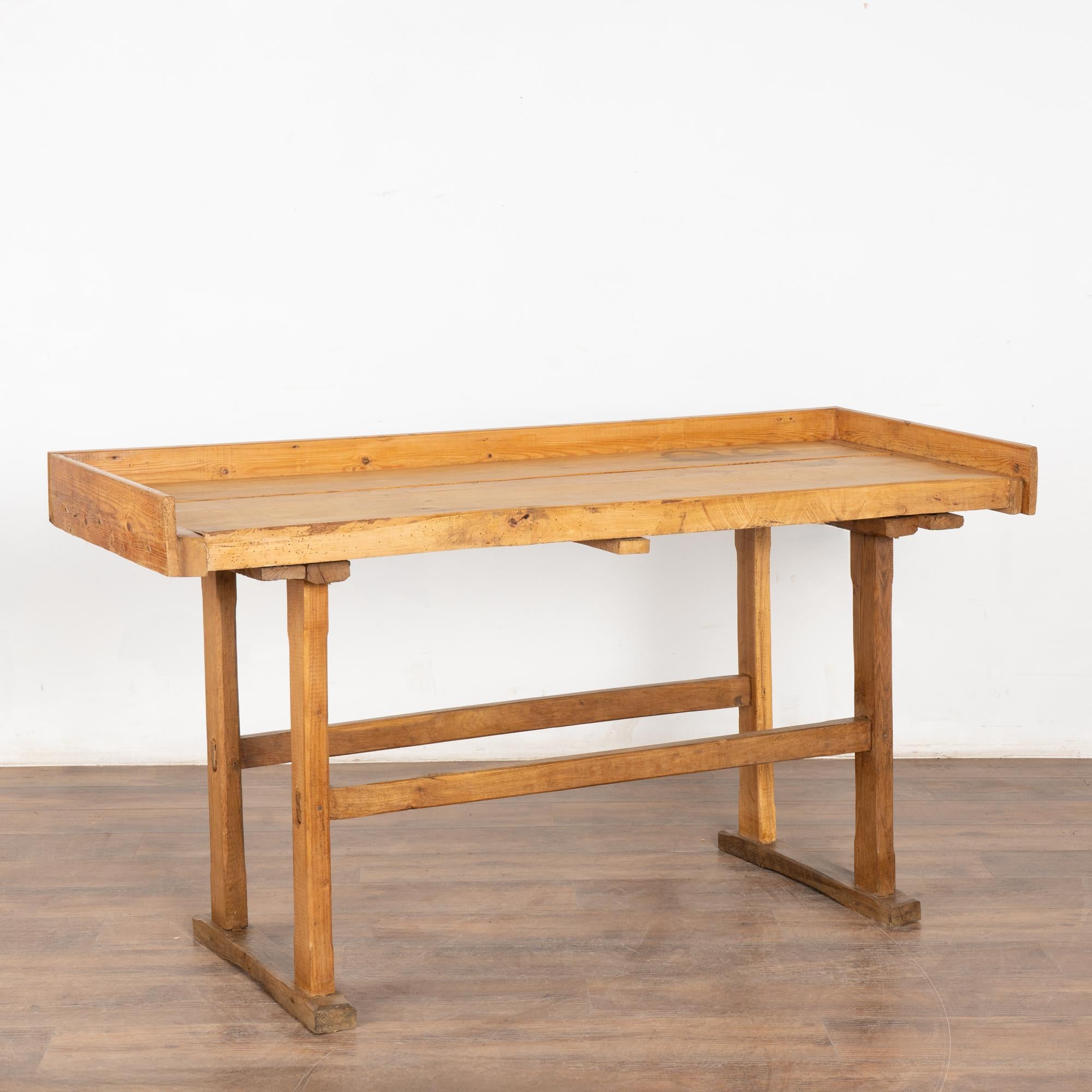 The appeal of this rustic pine console table comes from the well worn top reflecting generations of use.
It originally served as a work table, resulting in the worn patina with gouges, cracks, scrapes, stains, and age related separation of the