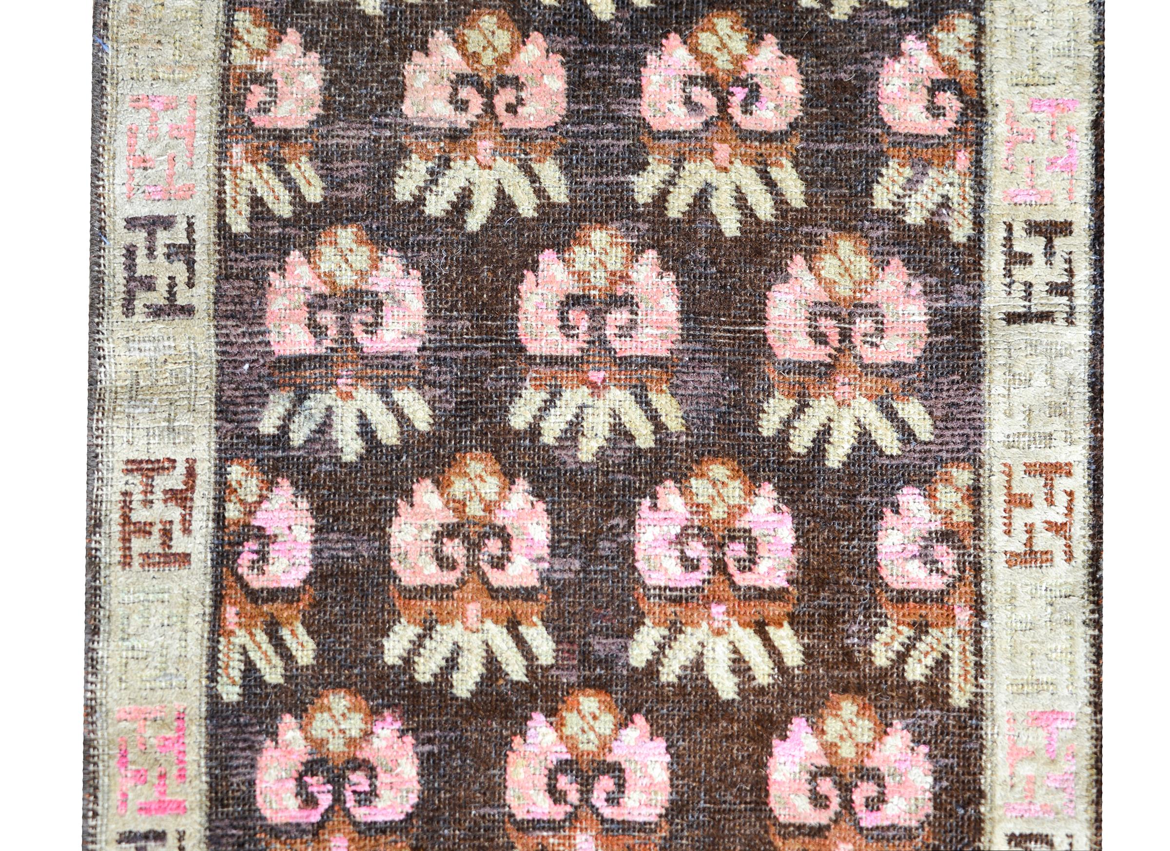 A wonderful early 20th century Central Asian Samarkand rug with an all-over stylized floral pattern woven in pink and gold and set against a dark brown background. The border is simple with a stylized meandering motif pattern.