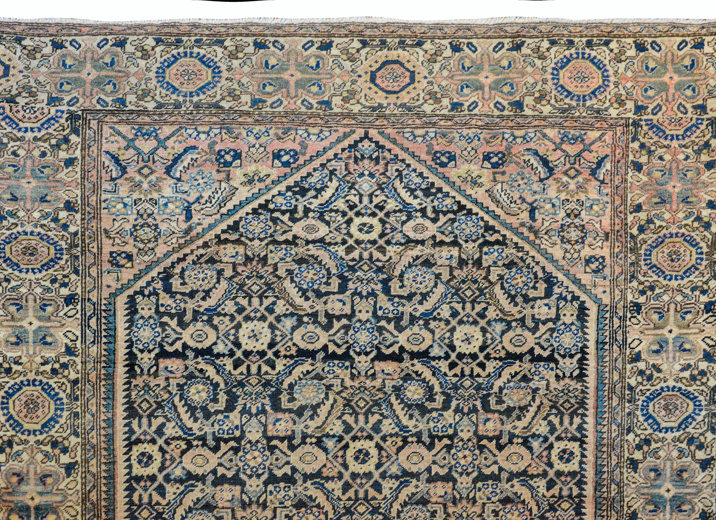 An outstanding early 20th century Persian Sarouk Farahan rug has been antique washed with a large central diamond woven in with a trellis leaf and flower pattern and woven in pale pink, gold, and light indigo, against an abrash dark indigo