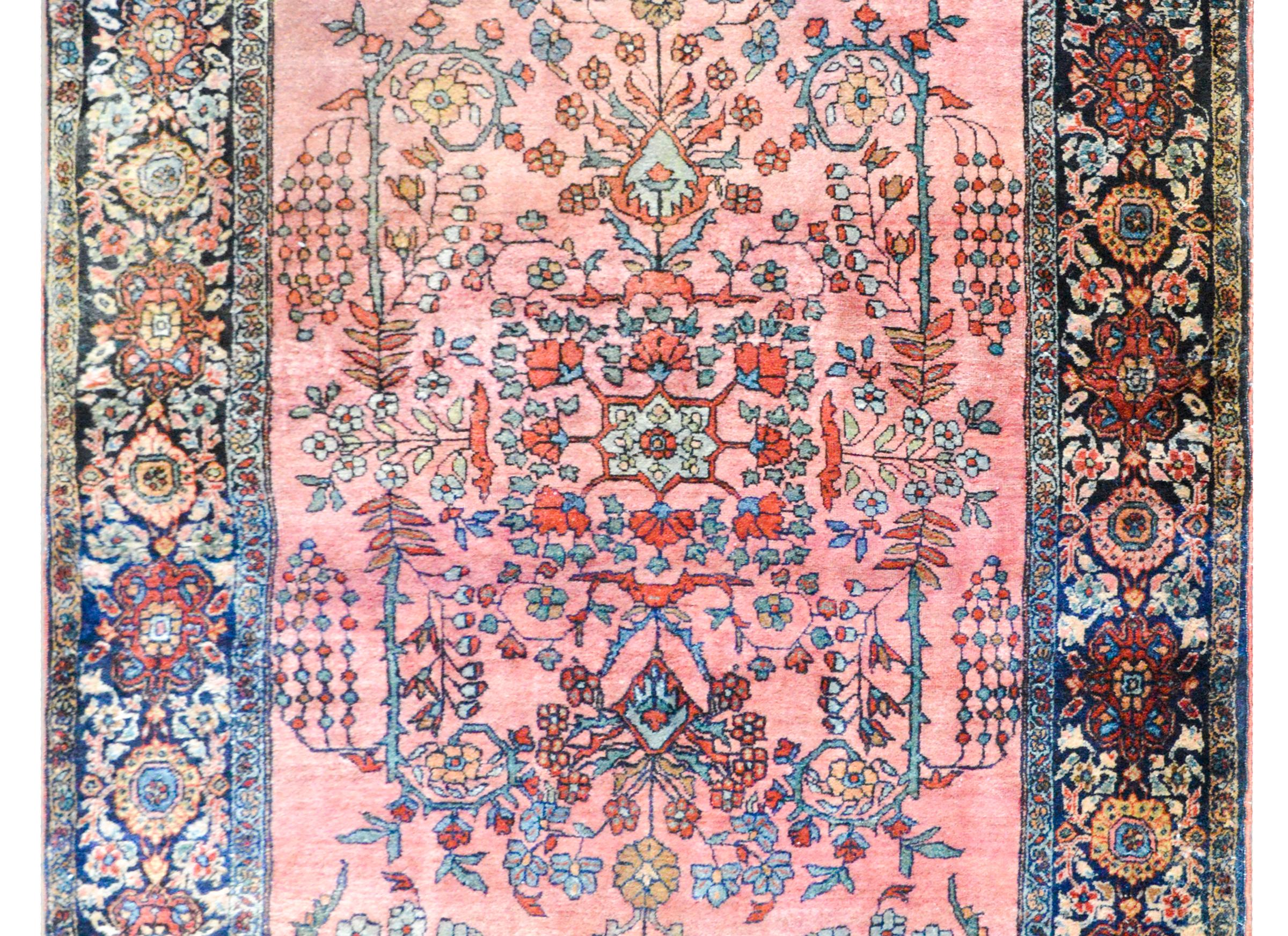 A wonderful early 20th century Persian Sarouk Farahan rug with a beautiful mirrored floral pattern woven in coral, light indigo, and gold against a pink background, and surrounded by a wide border with a large-scale repeated floral pattern woven in