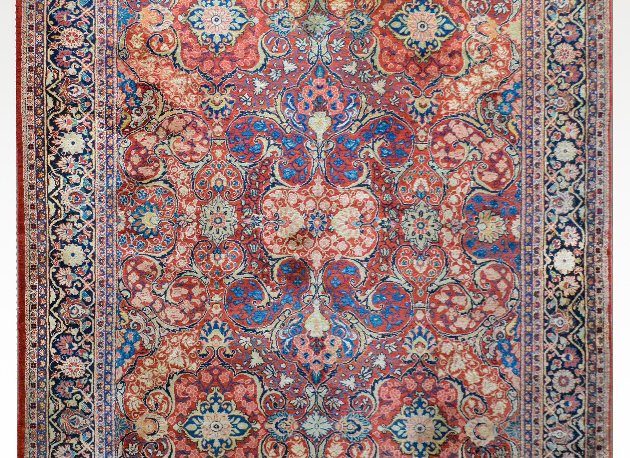 An outstanding early 20th century Persian Sarouk Mahal rug woven with a fantastic large-scale mirrored pattern of flowers and leaves woven in light and dark indigo, cream, crimson, pink, and gold on a cranberry background surrounded by a wonderful