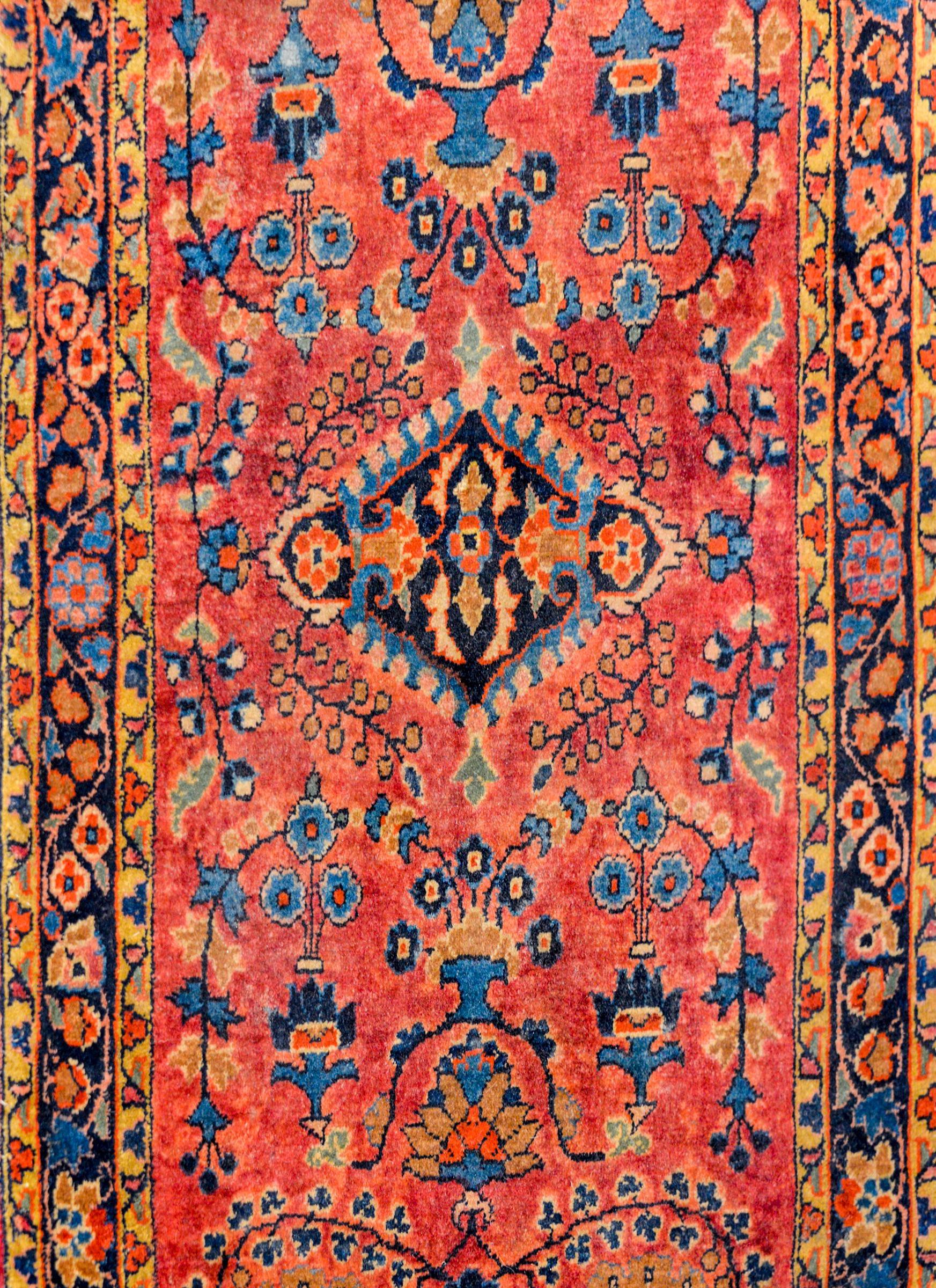 An early 20th century Persian Sarouk Mohajeran rug with a wonderful mirrored floral and vine pattern, woven in light and dark indigo, gold, pink, and crimson on a cranberry colored background. The border is simple, with a thin floral patterned
