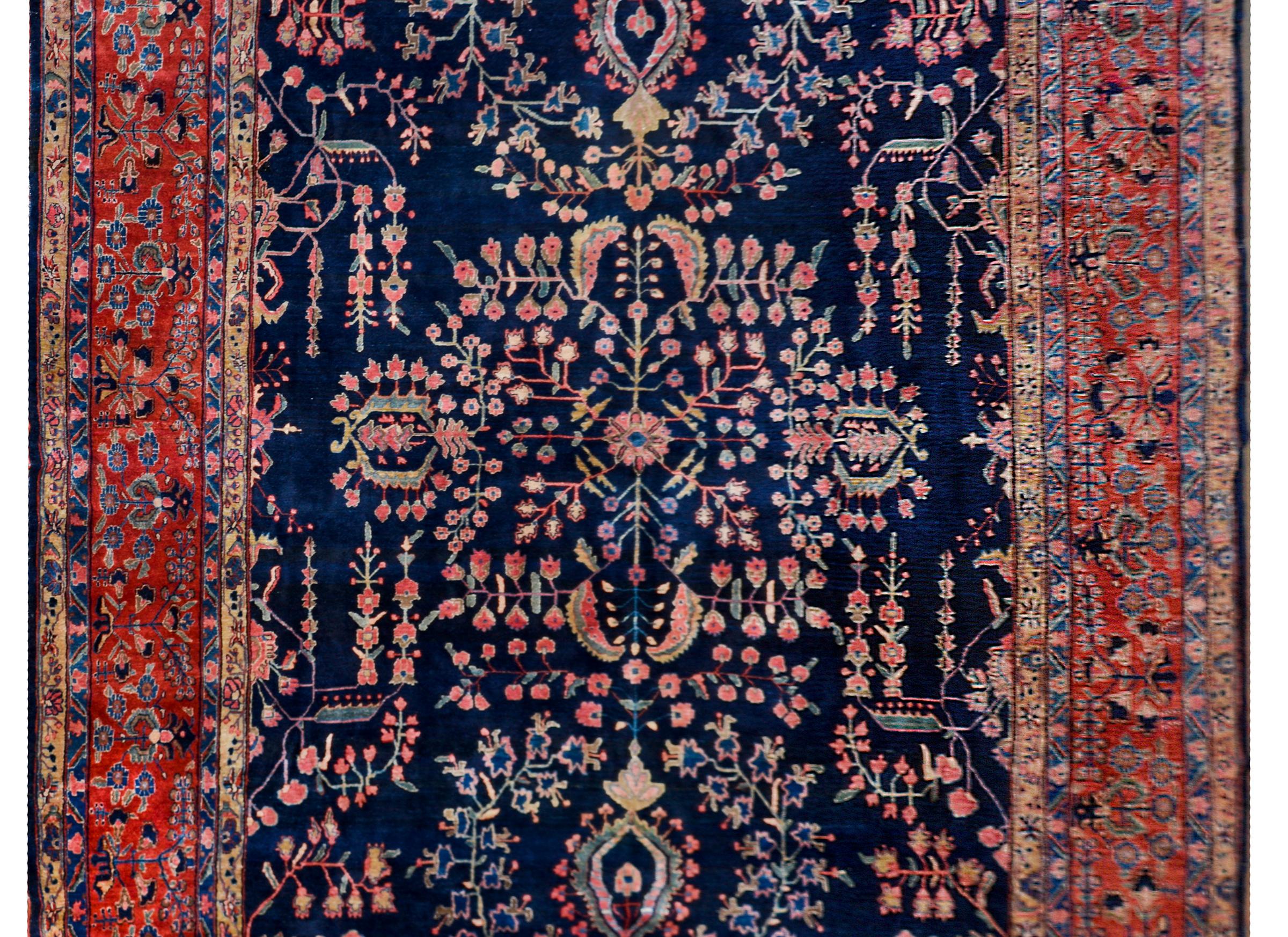 An incredible early 20th century Persian Sarouk Mohajeran rug with a traditional mirrored floral pattern woven in crimsons, pinks, creams, and indigos, against a dark indigo background. The border is complex with multiple floral patterned stripes