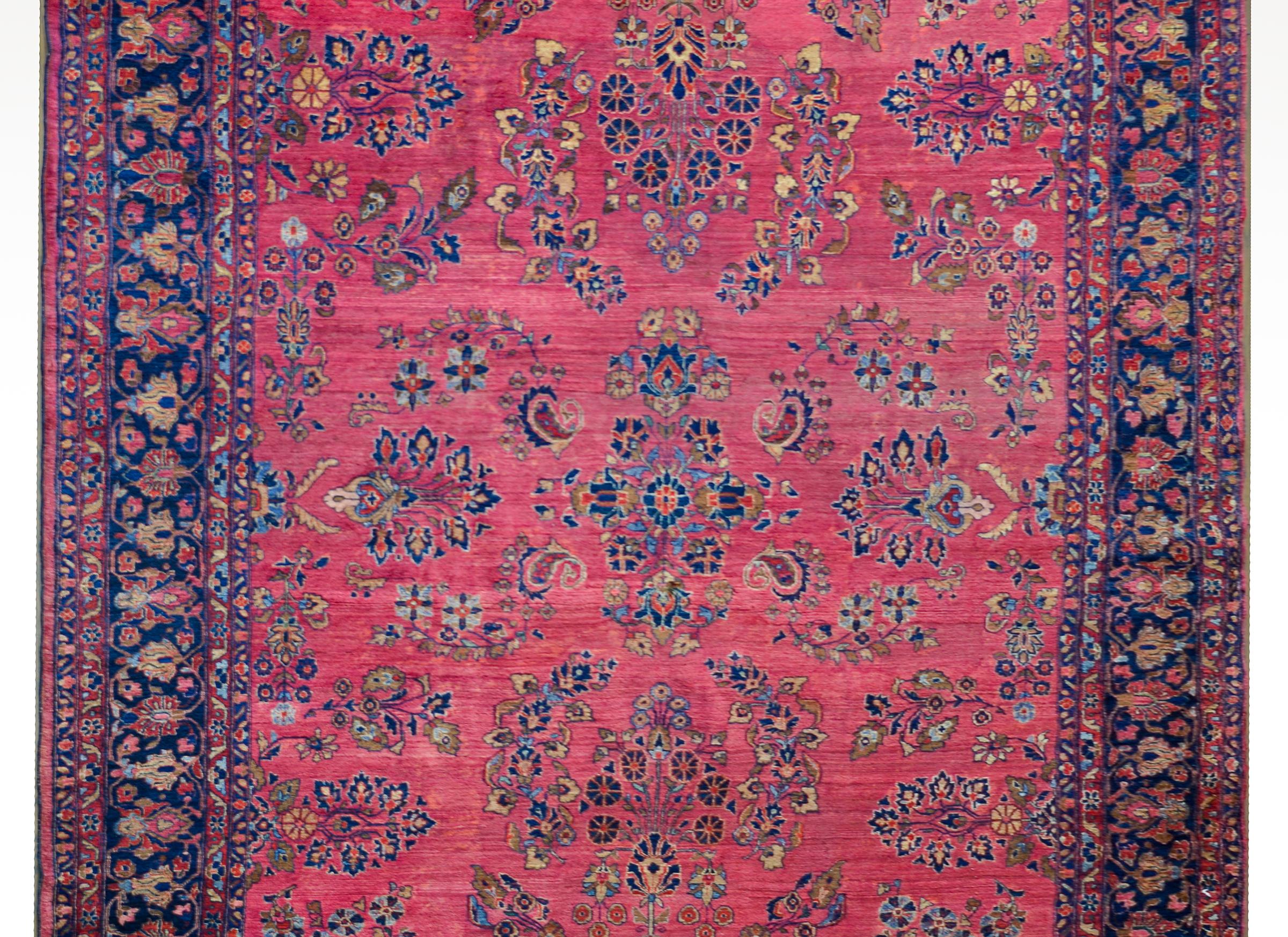 An incredible early 20th century Persian Sarouk Mohajeran rug with an all-over mirrored floral cluster pattern woven in traditional Sarouk colors of light and dark indigo, pink, cream, and red, against a cranberry colored background, and surrounded
