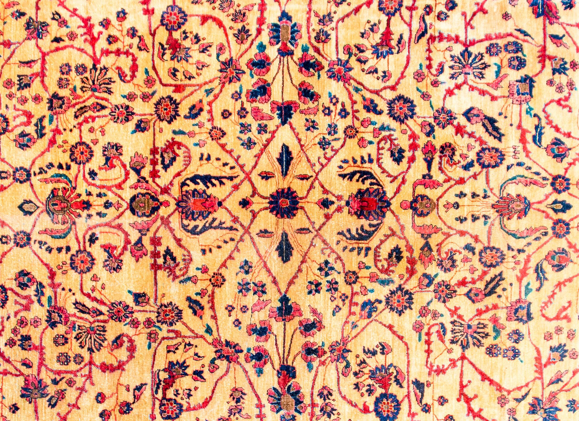 Ein persischer Sarouk-Teppich aus dem frühen 20. Jahrhundert mit einem schönen, gespiegelten, fein gewebten Blumen- und Rankenmuster in Indigo, Rosa und Karminrot auf einem gelben, pflanzengefärbten Wollgrund. Die Bordüre kontrastiert mit einem