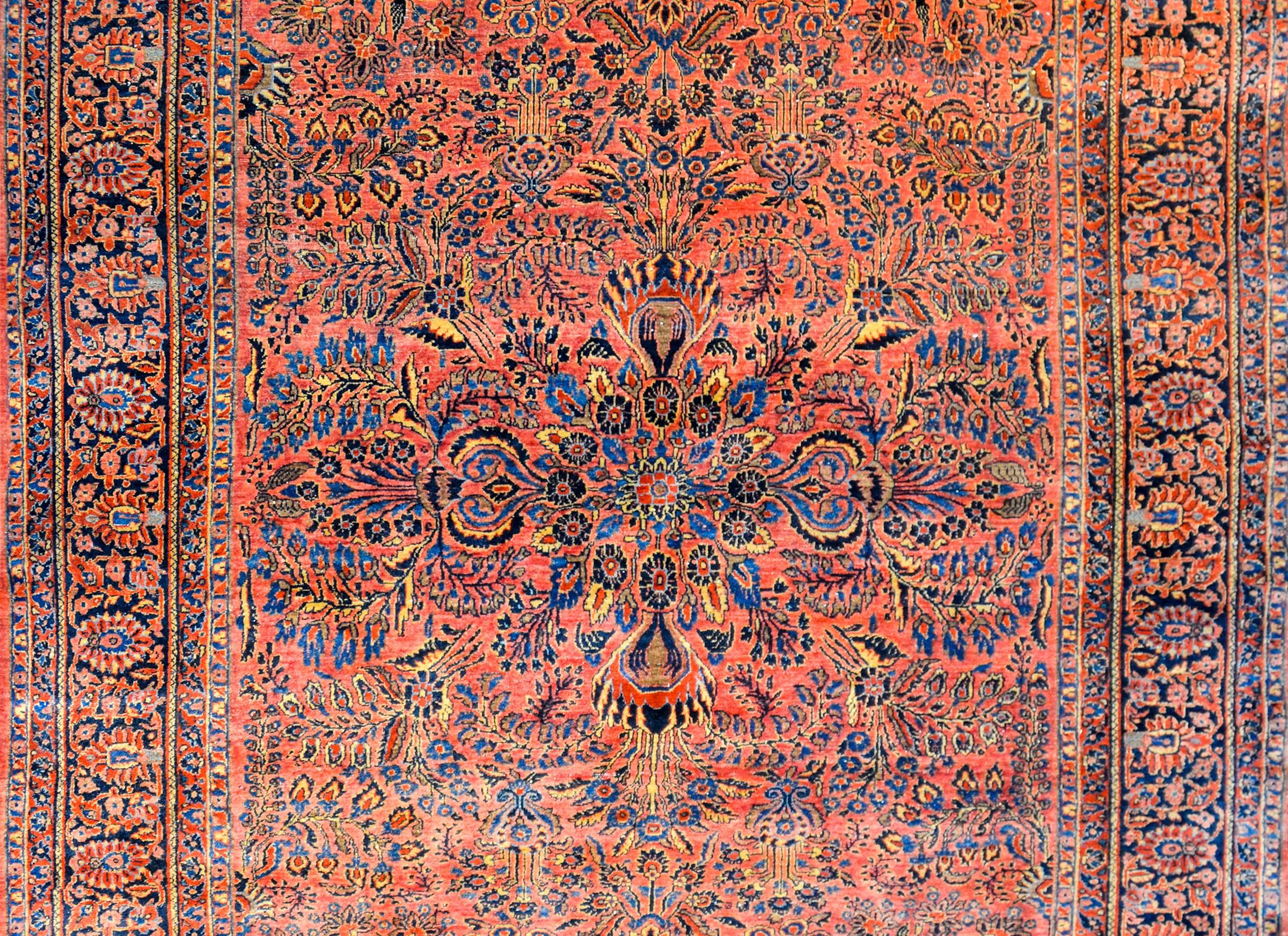 A beautiful early 20th century Persian Sarouk rug with a fantastic mirrored floral and vine pattern, expertly rendered, in light and dark indigo, salmon, gold, on a bold crimson background. The border is wide, with a wide stripe containing a floral