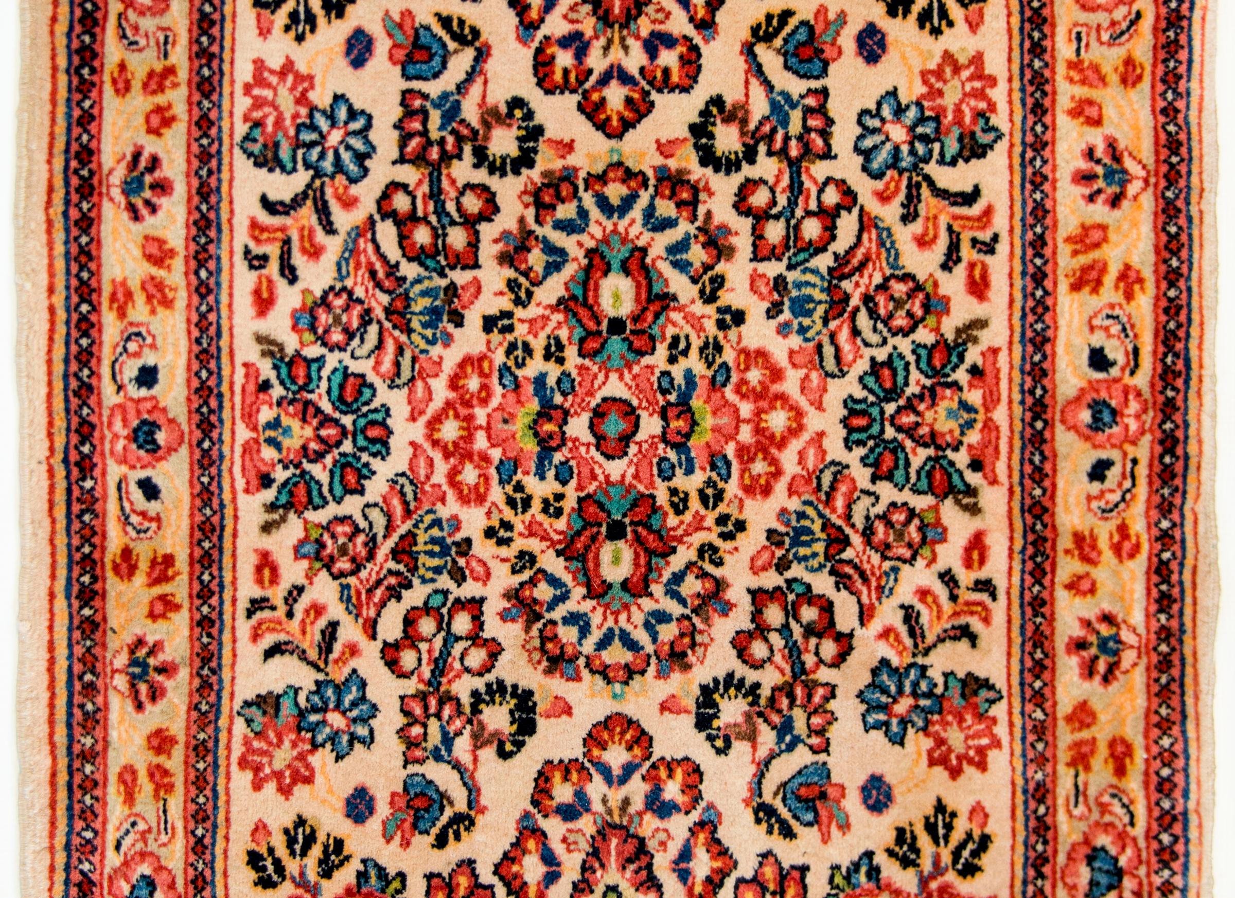 An early 20th century Persian Sarouk rug with an all-over mirrored multicolored pattern with myriad flowers woven in dark and light indigo, crimson, and gold on a white background. The border is composed of a wide floral patterned stripe flanked by