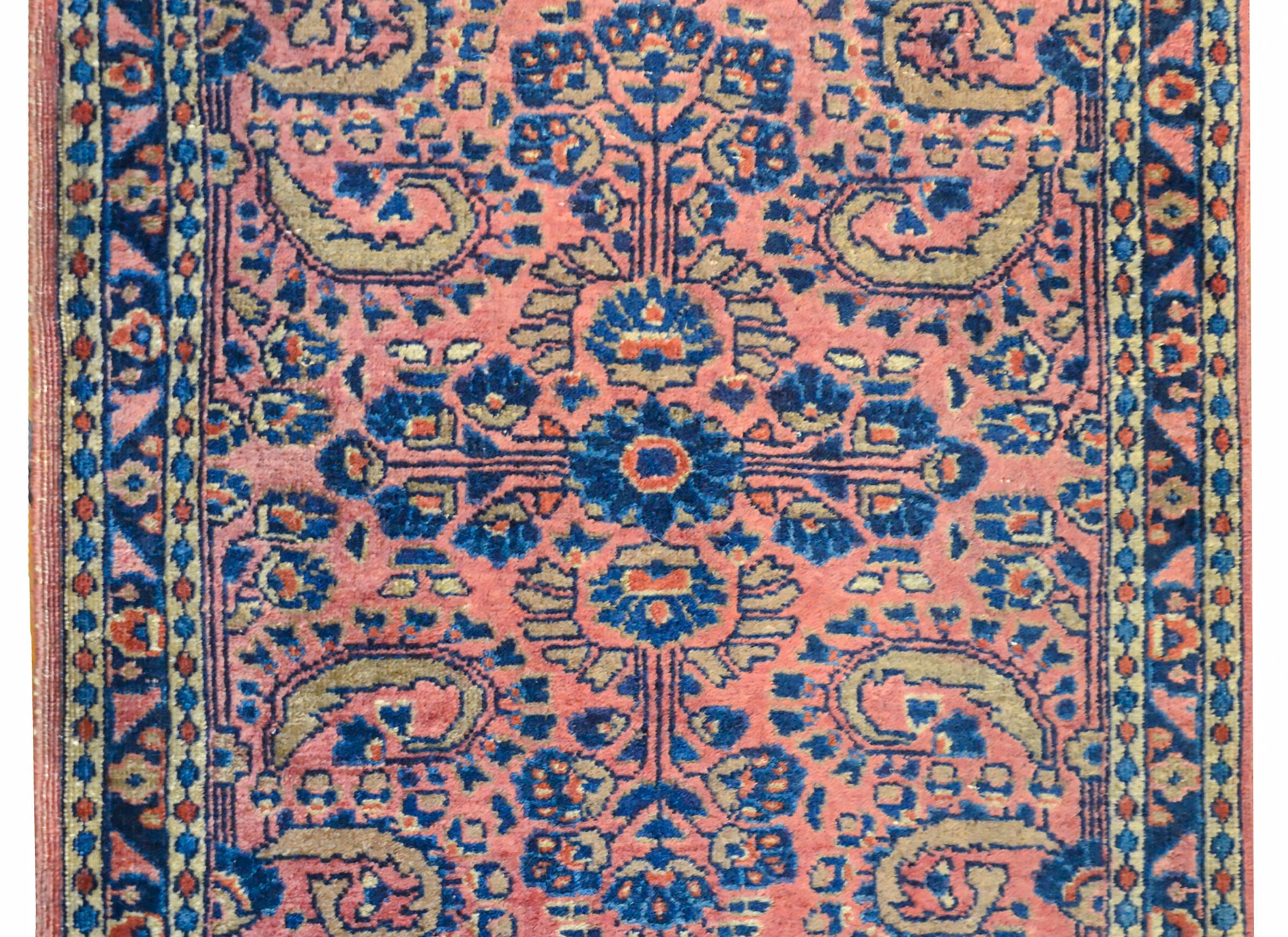 A wonderful early 20th century Persian petite Sarouk rug with a beautiful floral and scrolling vine pattern woven in light and dark indigo, gold, and coral on a pale coral background. The border is composed of a central floral patterned stripe
