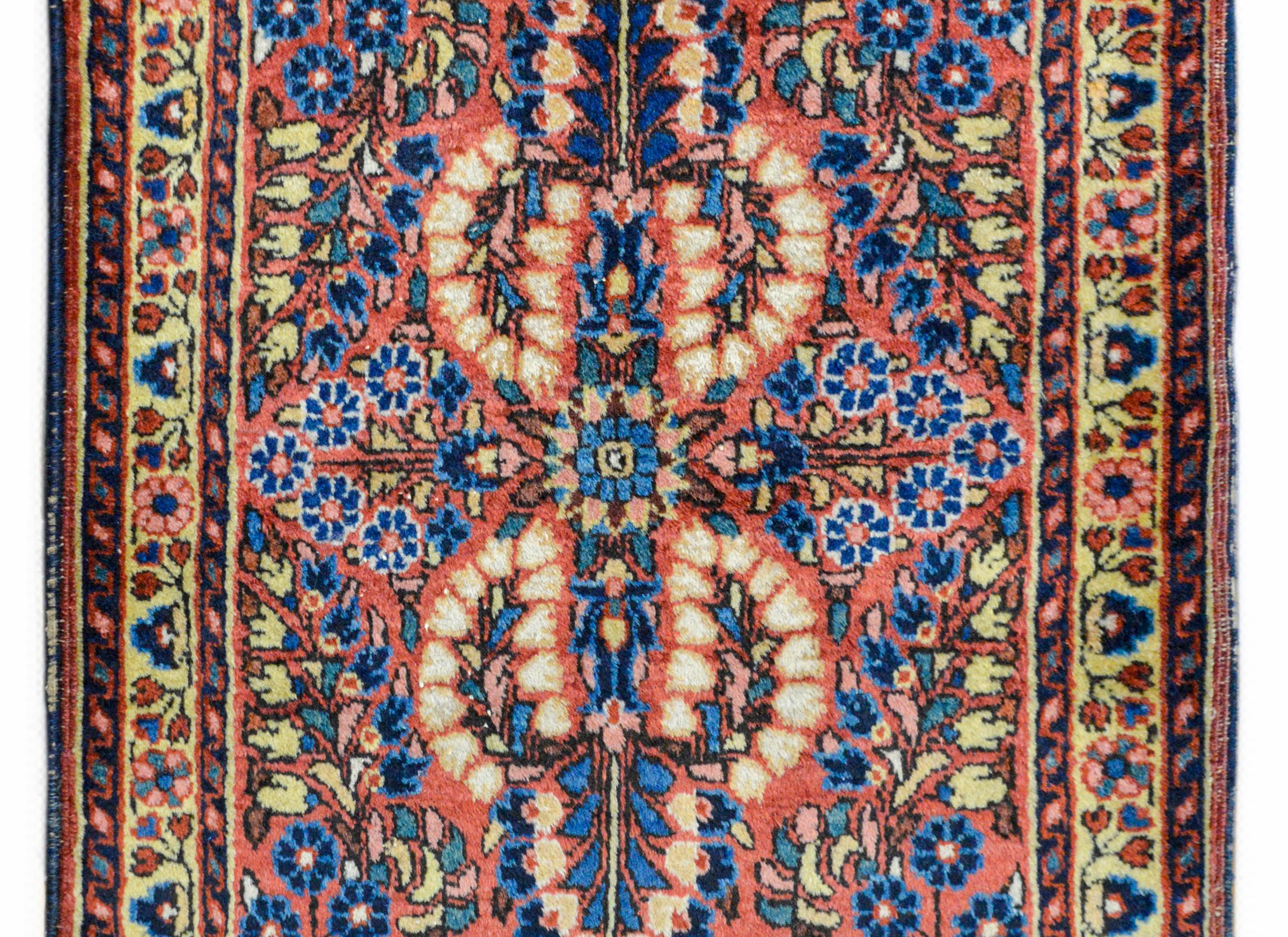 A charming early 20th century Persian Sarouk rug with a mirrored floral pattern woven in myriad colors against a coral colored background, and surrounded by a border containing a wide floral pattered central stripe flanked by a pair of petite floral