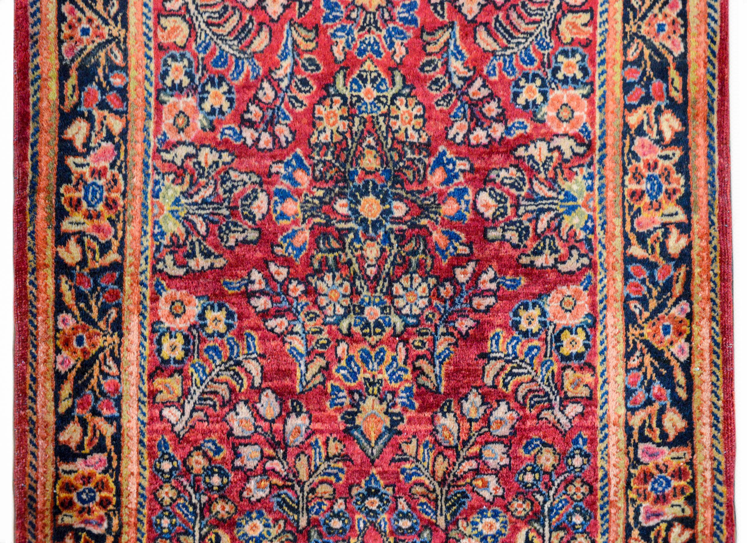 A beautiful early 20th century Persian Sarouk rug with a mirrored floral pattern woven in pink, light and dark indigo, cream, and brown against a cranberry colored background. The border is wide with a large floral partnered central stripe flanked