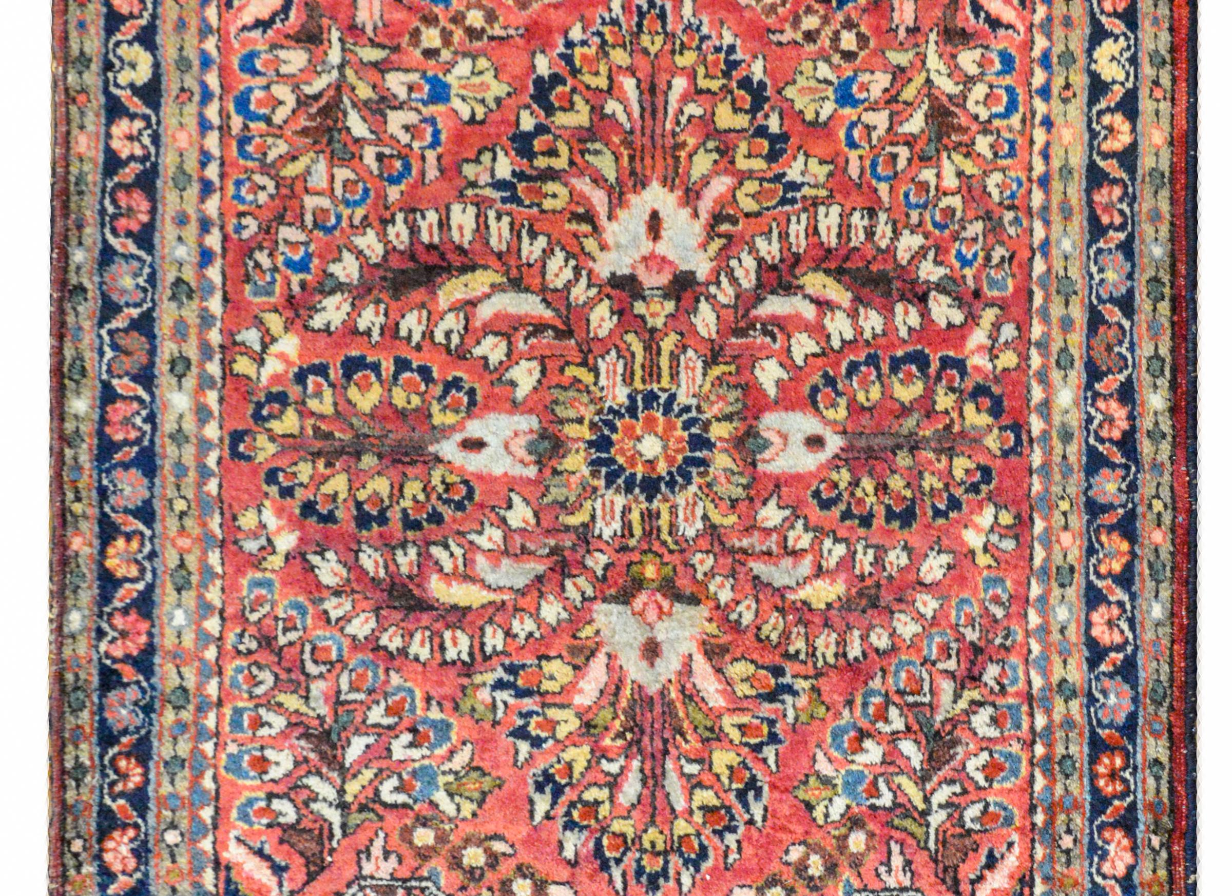 A wonderful early 20th century petite Persian Sarouk rug with a large-scale mirrored floral pattern woven in light and dark indigo, cream, pink, and green wool, against a light cranberry colored ground. The border is sweet with a central petite