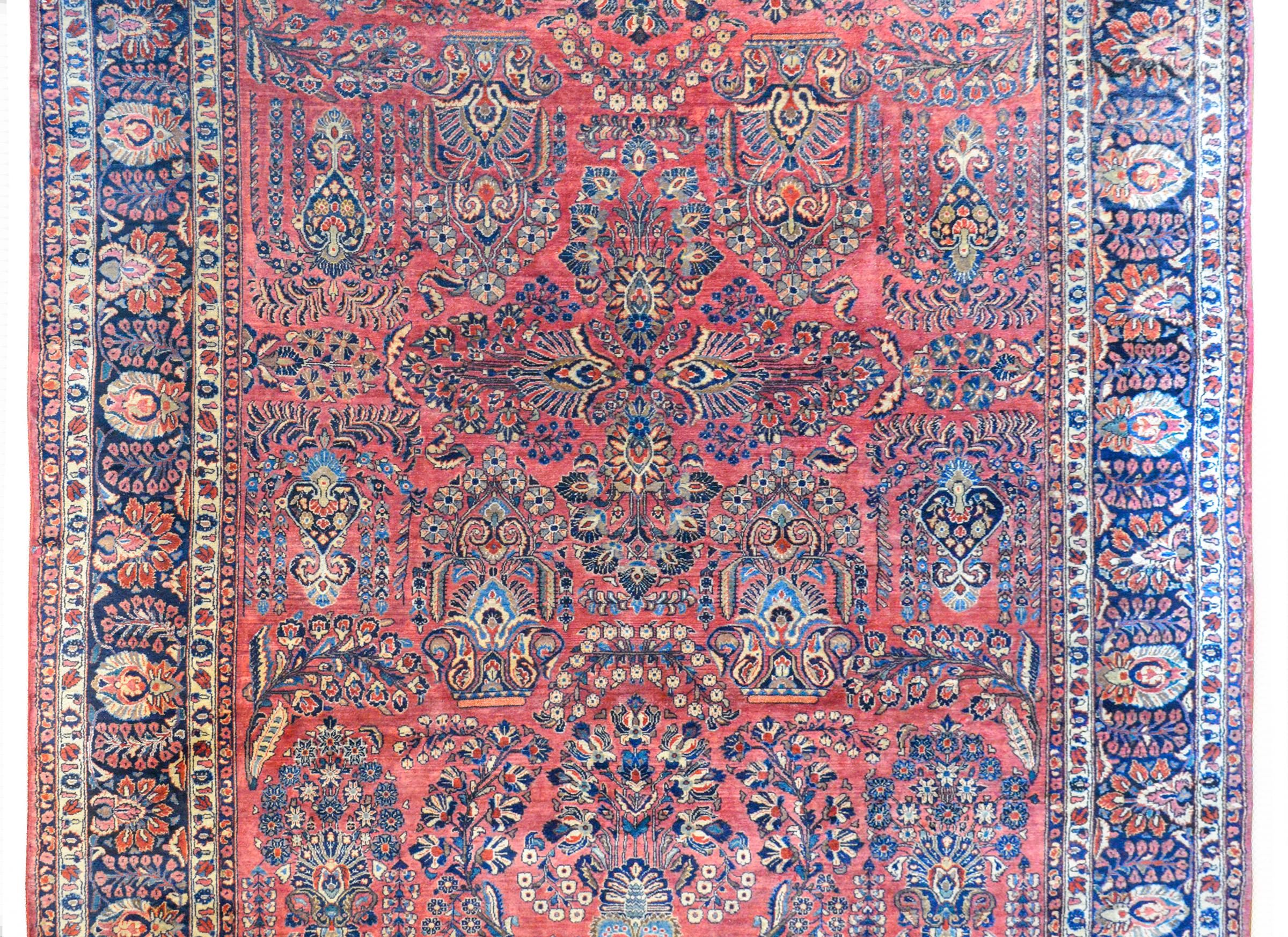 A fantastic early 20th century Persian Sarouk with the most beautiful large-scale mirrored floral and leaf pattern woven in traditional Sarouk colors of light and dark indigo, cream, and pink against a rich cranberry ground. The border is amazing