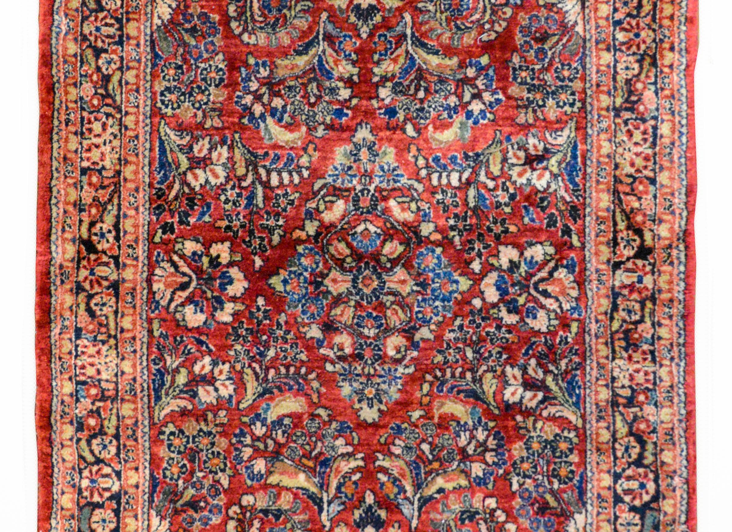 A gorgeous early 20th century Persian Sarouk rug with an all-over pattern containing several large flower clusters woven in indigo, pink, green, and white, against a dark cranberry background. The border is wonderful with a central floral patterned