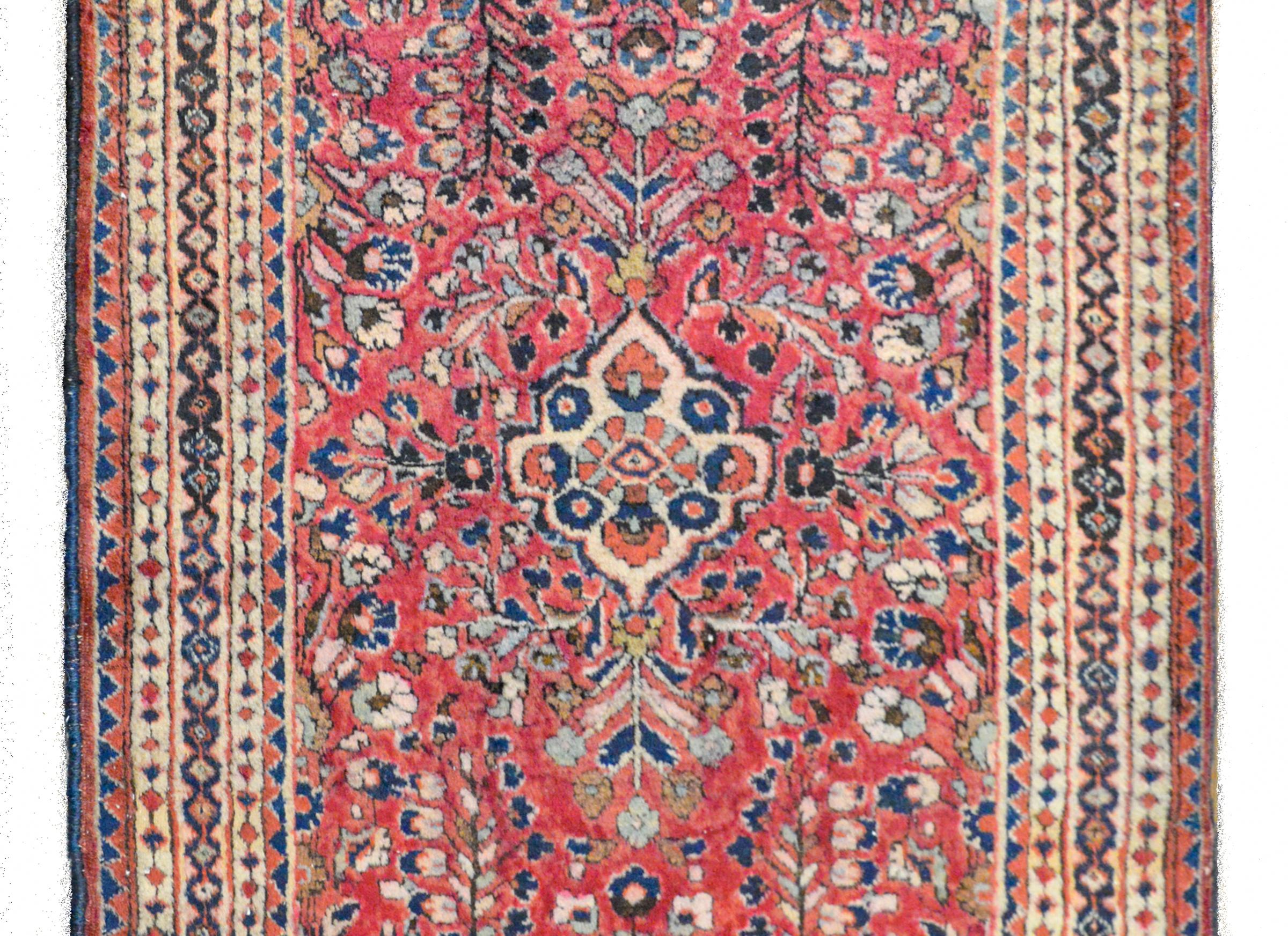A fantastic early 20th century Persian Sarouk rug with a mirrored floral patterned field woven in pink, light and dark indigo, brown, and coral colored wool, and surrounded by a wide border containing multiple geometric pattered stripes.