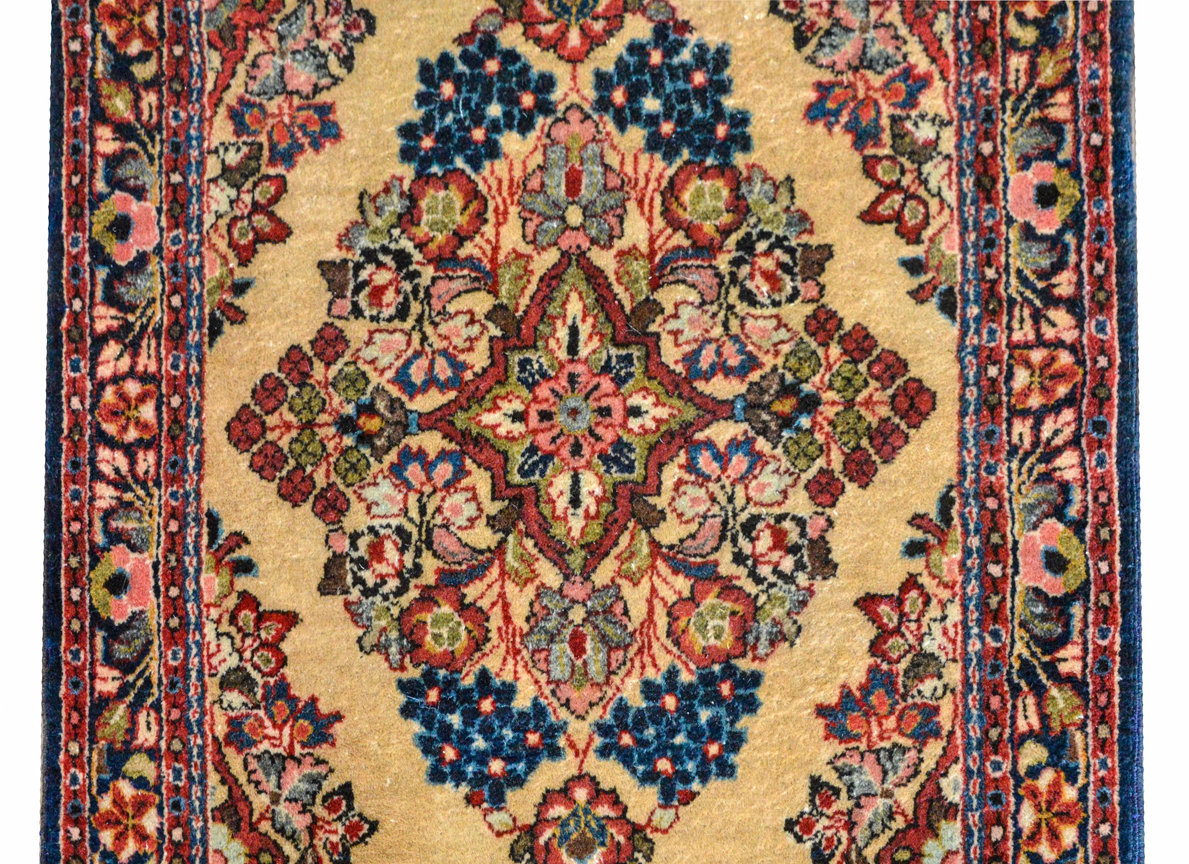 A wonderful early 20th century Persian Sarouk rug woven with a central floral medallion woven in light and dark indigo, green, pink, and cream, set against a champagne colors background, and surrounded by a border woven with similar flowers as the