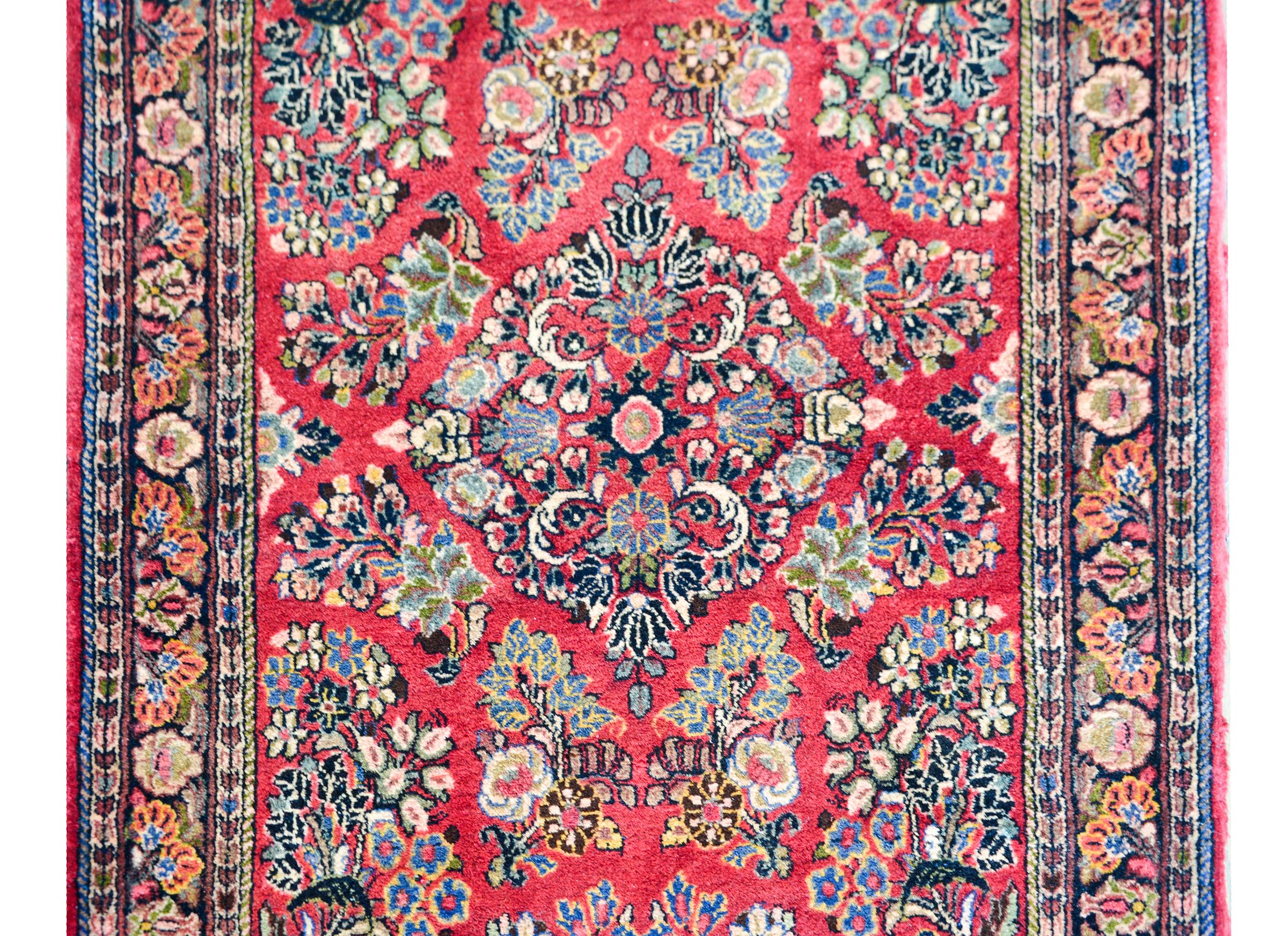 A beautiful early 20th century Persian Sarouk runner with an all-over mirrored floral cluster pattern woven in myriad colors and surrounded by a border with multiple thin floral patterned stripes.