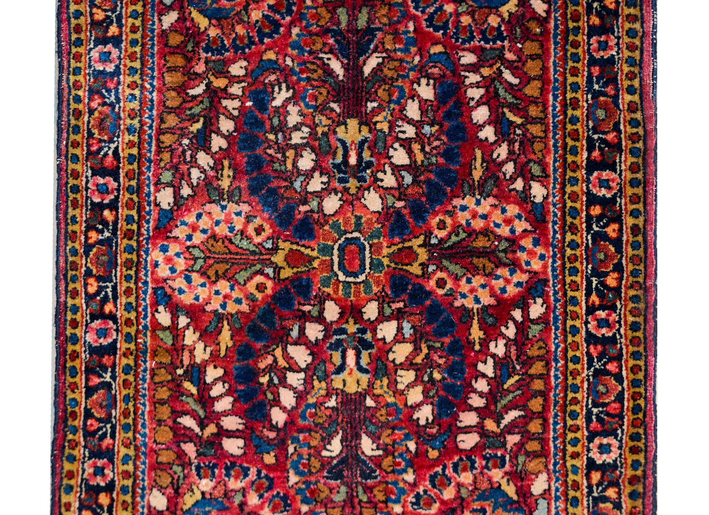 A striking early 20th century Persian Sarouk rug with a mirrored all-over floral pattern woven in traditional colored of pink, indigo, white, gold, and teal, against a cranberry colored background. The border is simple with a central floral pattered