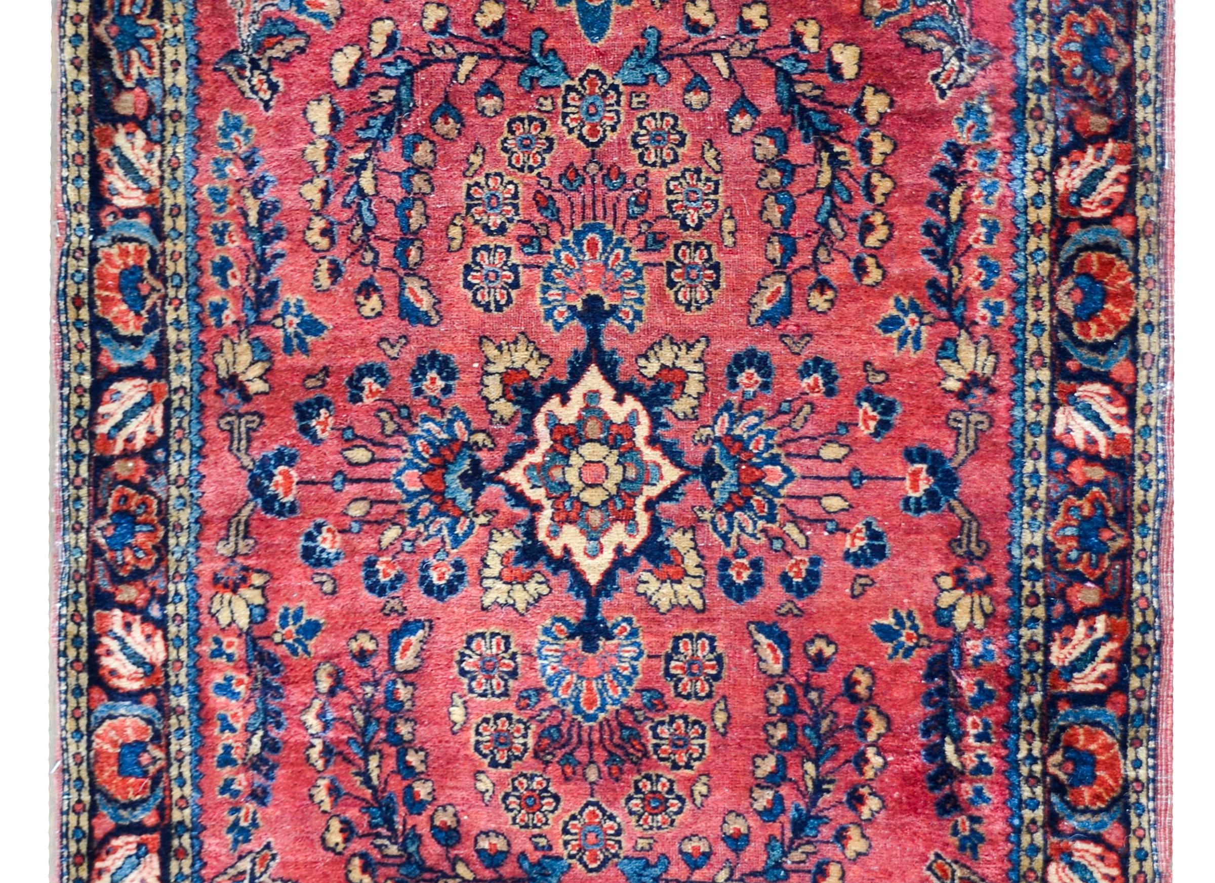A wonderful early 20th century Persian Sarouk rug with a traditional mirrored floral cluster pattern woven in light and dark indigo, cream, and crimson set against a coral background, and surrounded by a beautiful floral patterned border.