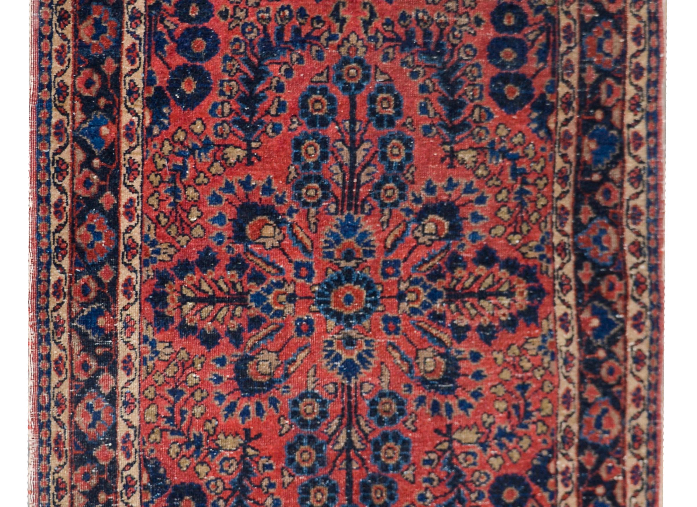 A beautiful early 20th century Persian Sarouk rug with a traditional mirrored floral pattern woven with myriad floral and scrolling vine clusters and surrounded by a border containing several petite floral pattered stripes, and all woven in light