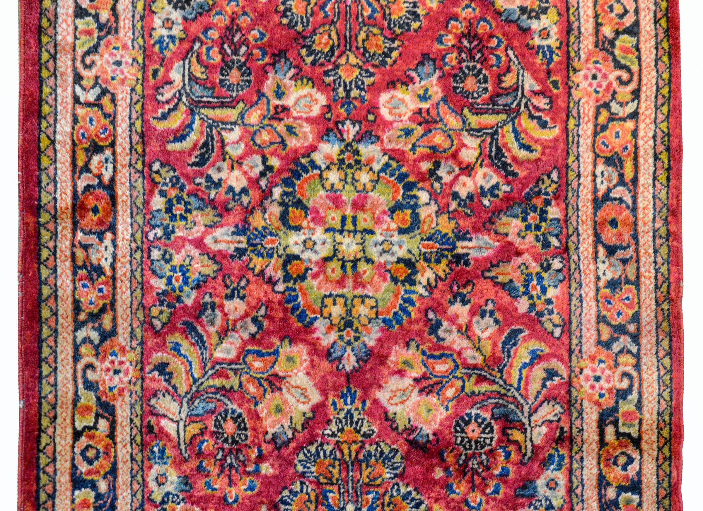 Beautiful early 20th century Persian Sarouk runner with an all-over mirrored floral pattern woven in cranberry, gold, pale green, and light and dark indigo, and surrounded by a simple scrolling vine and floral border.