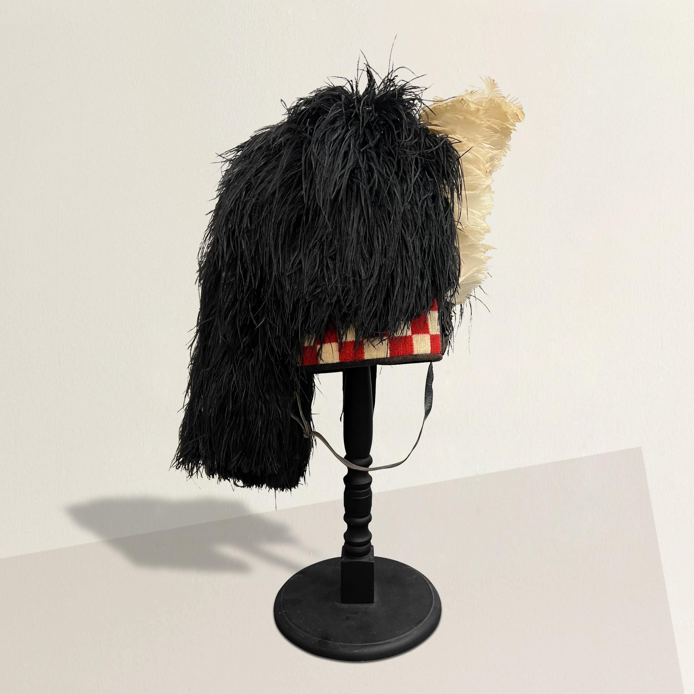 A playful yet strong early 20th century Scottish bagpiper's bonnet with a woven wool checkerboard headband and decorated with a large black ostrich feather plume and a white feather hackle, mounted on a turned wood stand.