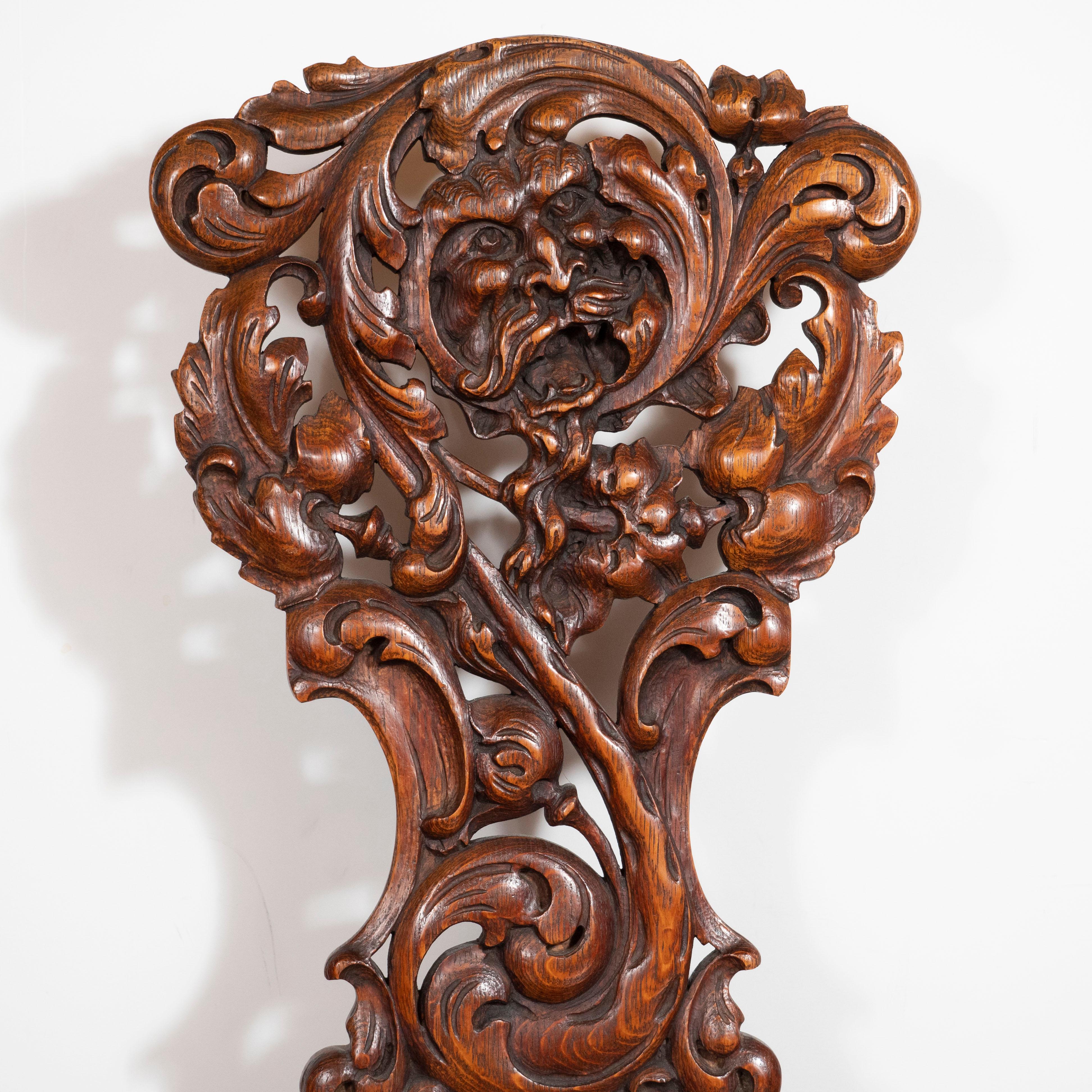 This elegant and dramatic side chair was hand carved in the United States, circa 1900. It features the carved face of a bearded male figure surrounded by swirling stylized foliate forms with a scalloped seat. Additionally, the piece offers