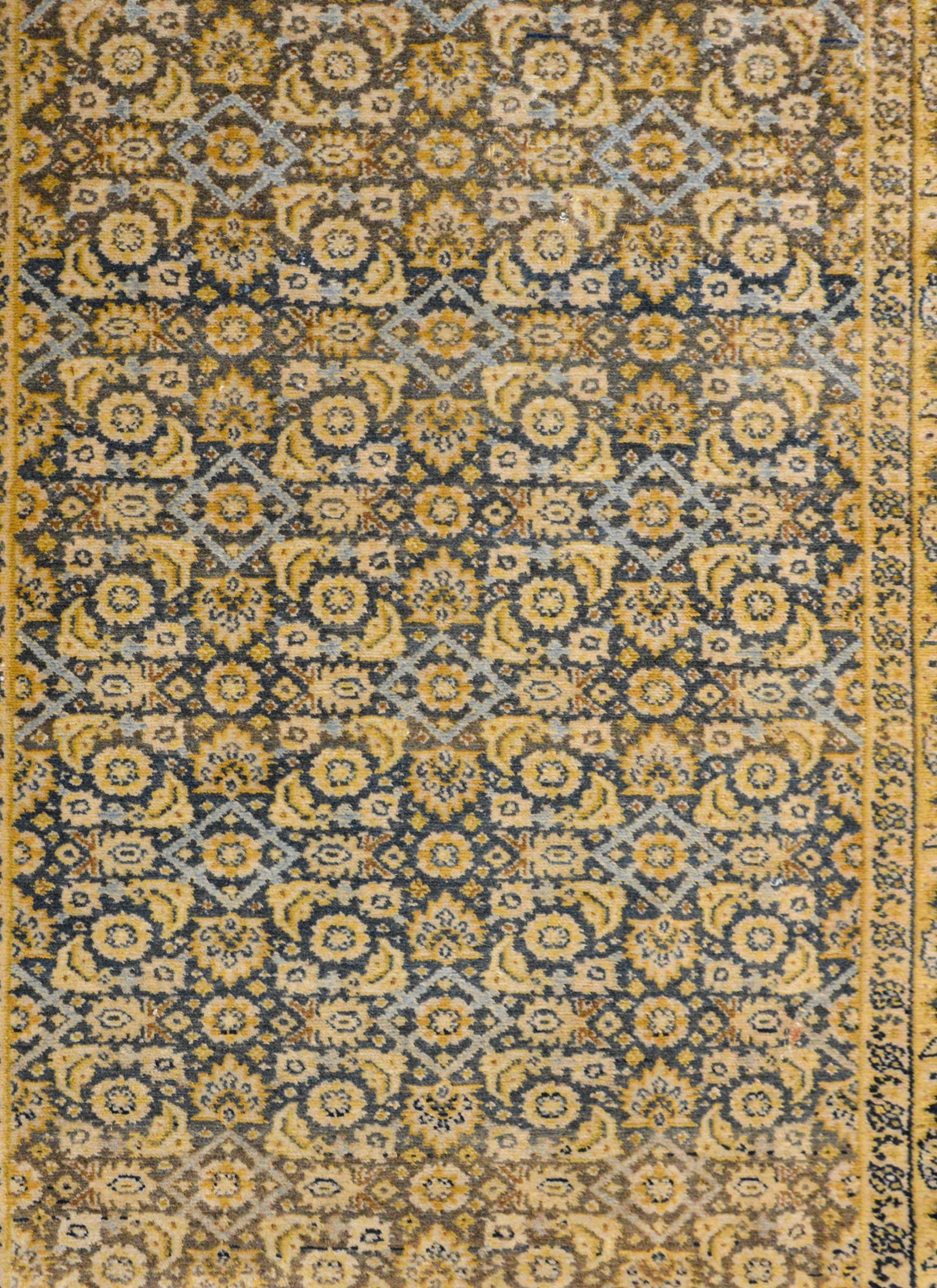 A beautiful early 20th century Persian Senneh rug with an all-over trellis pattern containing flowers and leaves woven in gold, cream, and light indigo on a dark indigo background. The border is wide with a central leaf patterned stripe flanked by a