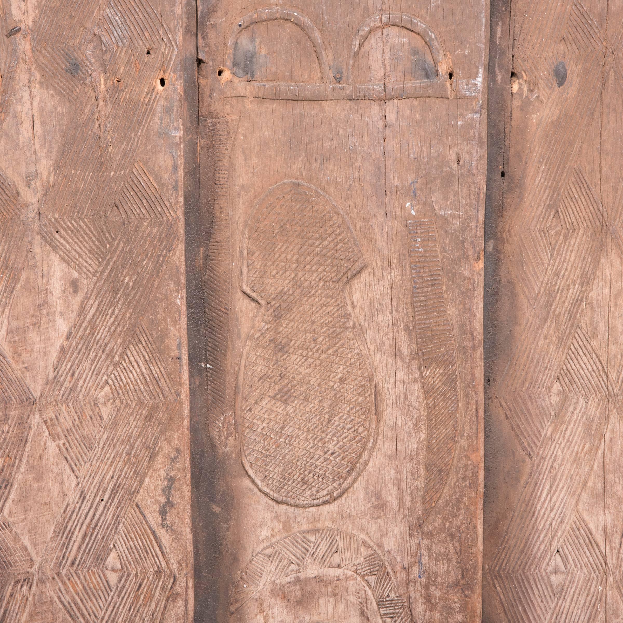 Notches in one plank of this traditional door speak to the hinge points that held it in place throughout its long life as the entryway of a Senufo home. The vertical planks alternate between abstract geometric design and potent symbolism. Carved out