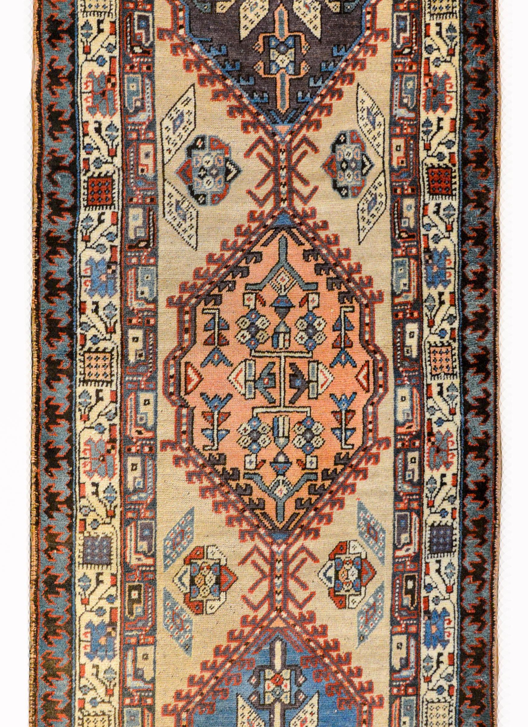 A fantastic early 20th century Persian Serab runner with six large diamond patterned medallions, each with a unique stylized floral pattern, woven in crimson, indigo, pink, and brown, and all set against a camel colored background. The border is