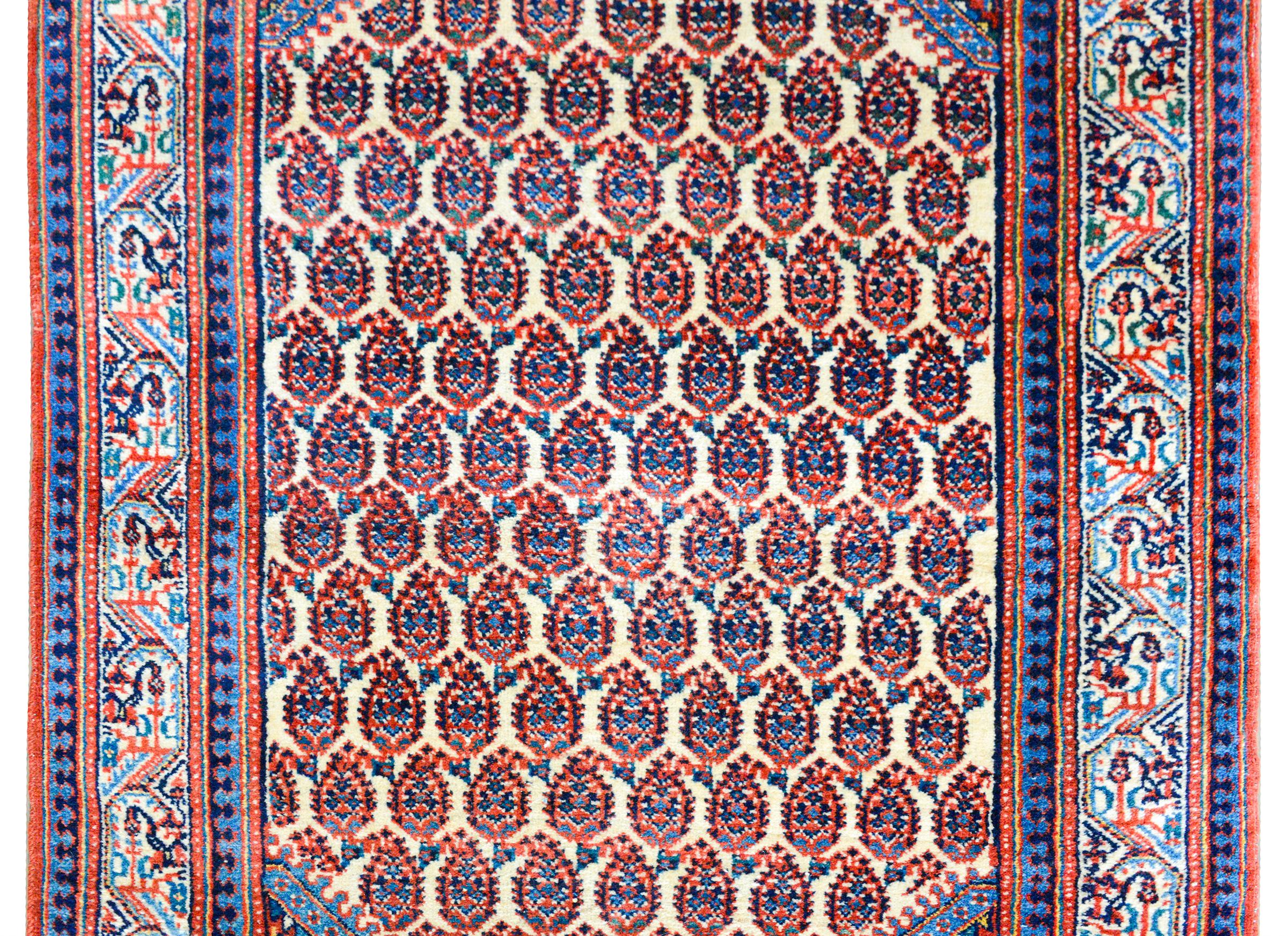 Ein bezaubernder persischer Seraband-Teppich aus dem frühen 20. Jahrhundert mit einem Allover-Paisleymuster in Karmesinrot sowie hellem und dunklem Indigo auf cremefarbenem Hintergrund, umgeben von einer schönen Bordüre mit einem zentralen