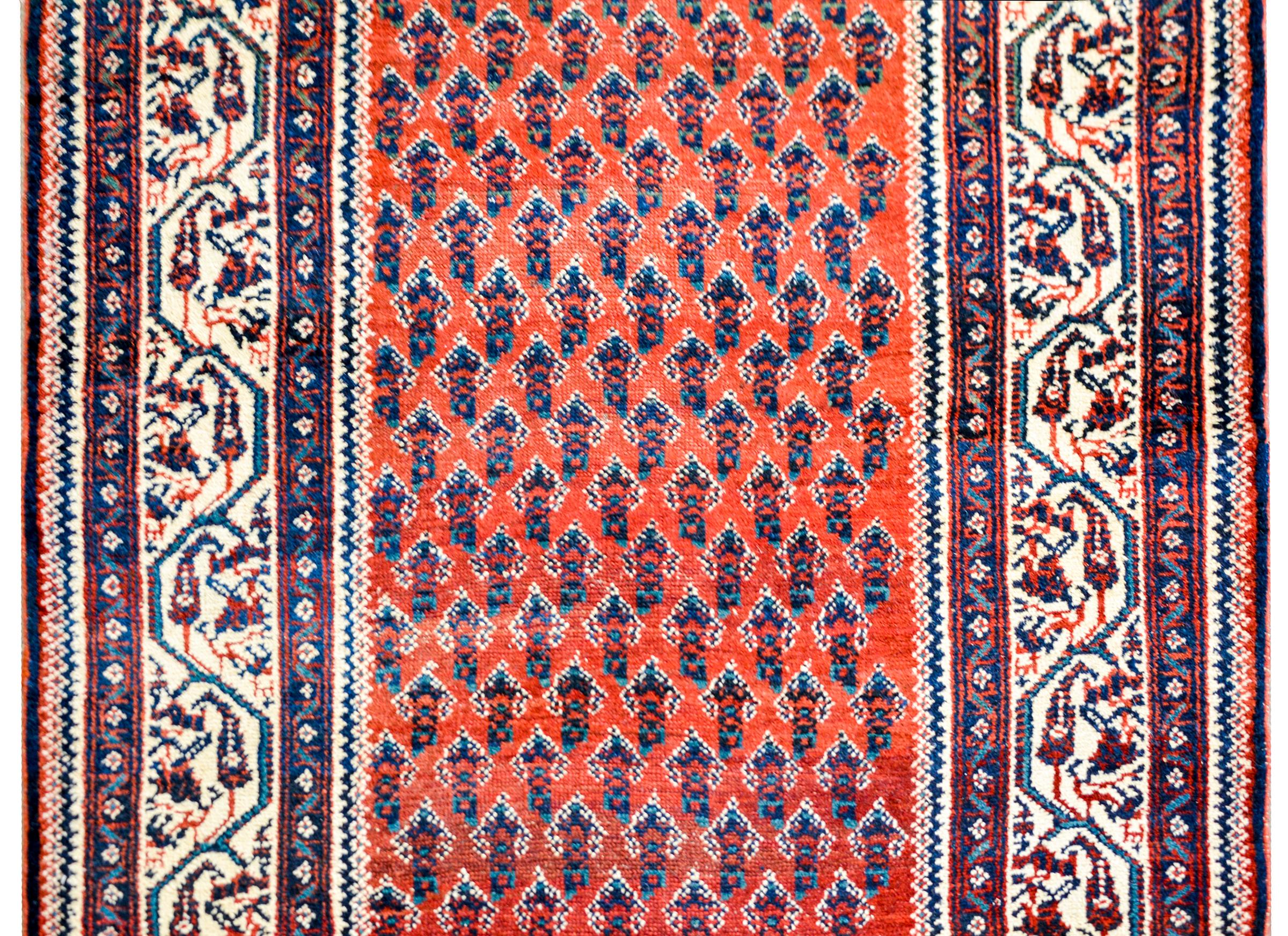 An early 20th century Persian Seraband runner with an all-over beautiful stylized paisley pattern woven in indigo, green, and crimson, on a crimson background surrounded by a fantastic border containing a wide central scrolling vine and paisley