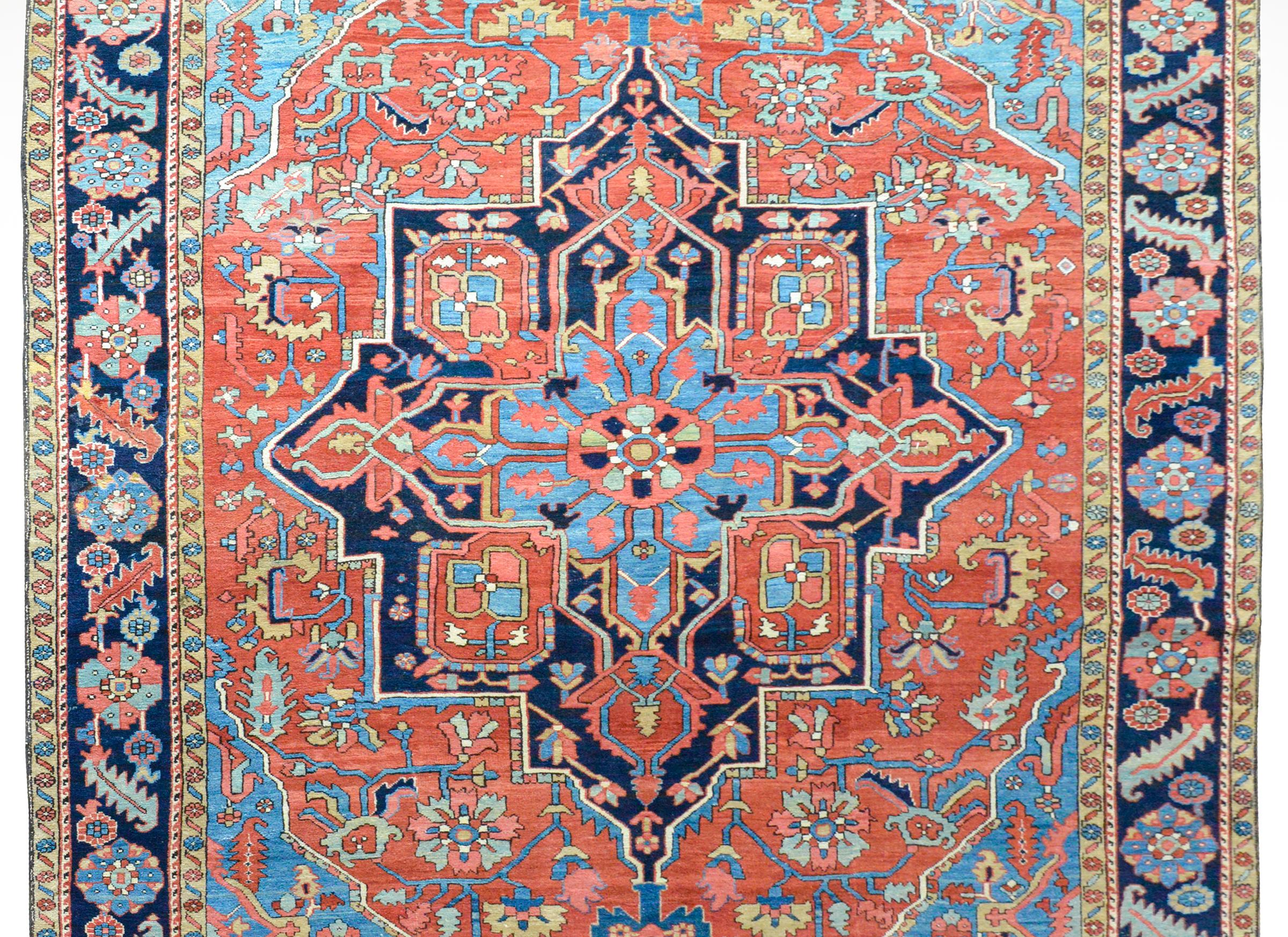 A fantastic early 20th century Persian Serapi rug with a traditional large-scale stylized floral medallion woven in light and dark indigo, pink, gold, and coral against a red background and surrounded by a wide border with a stylized floral pattern