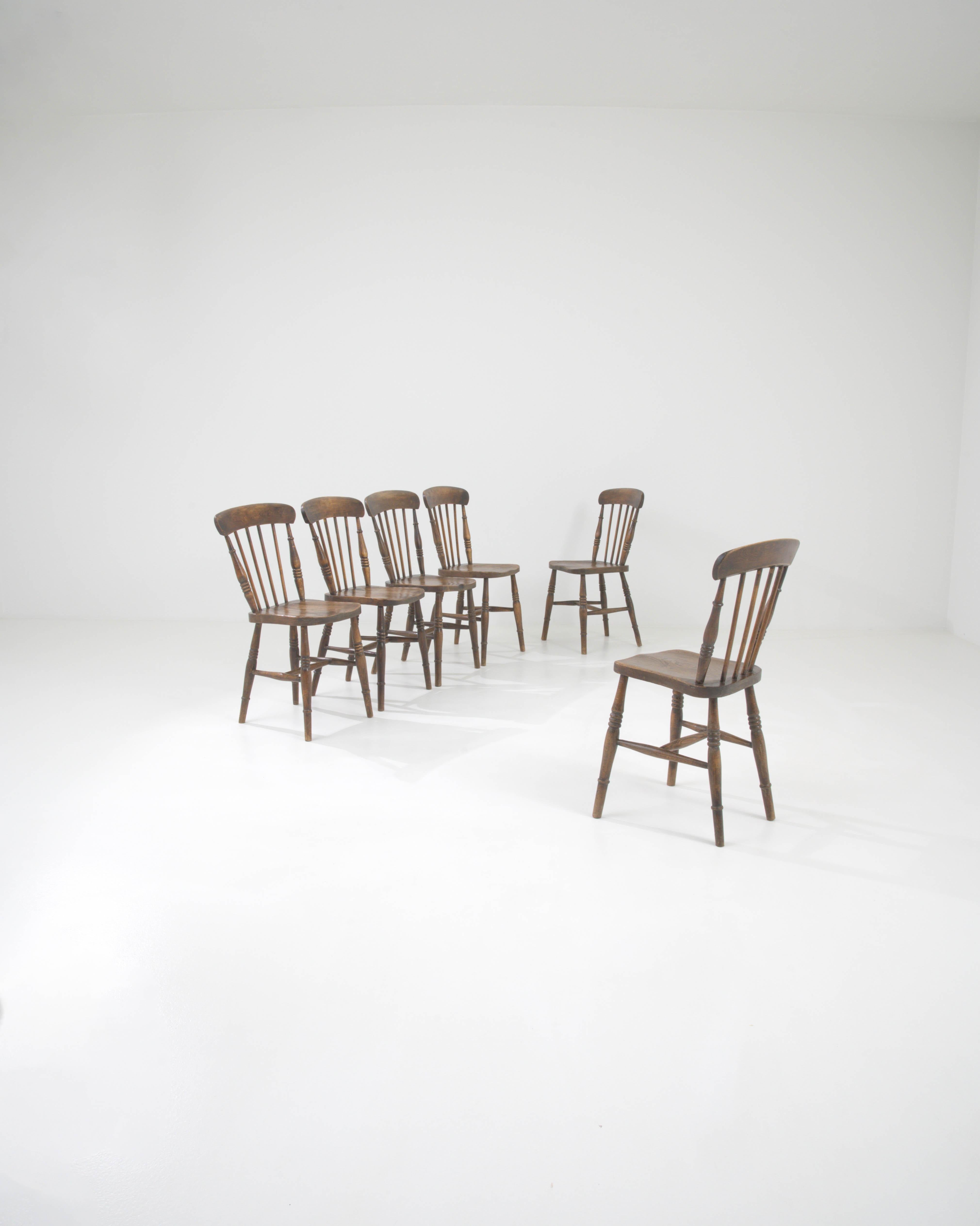 This exquisite set of wooden dining chairs from the early 20th century is steeped in the traditions of classic craftsmanship. Each chair in this collection stands as a testament to timeless design, featuring a curved top rail and slender spindles