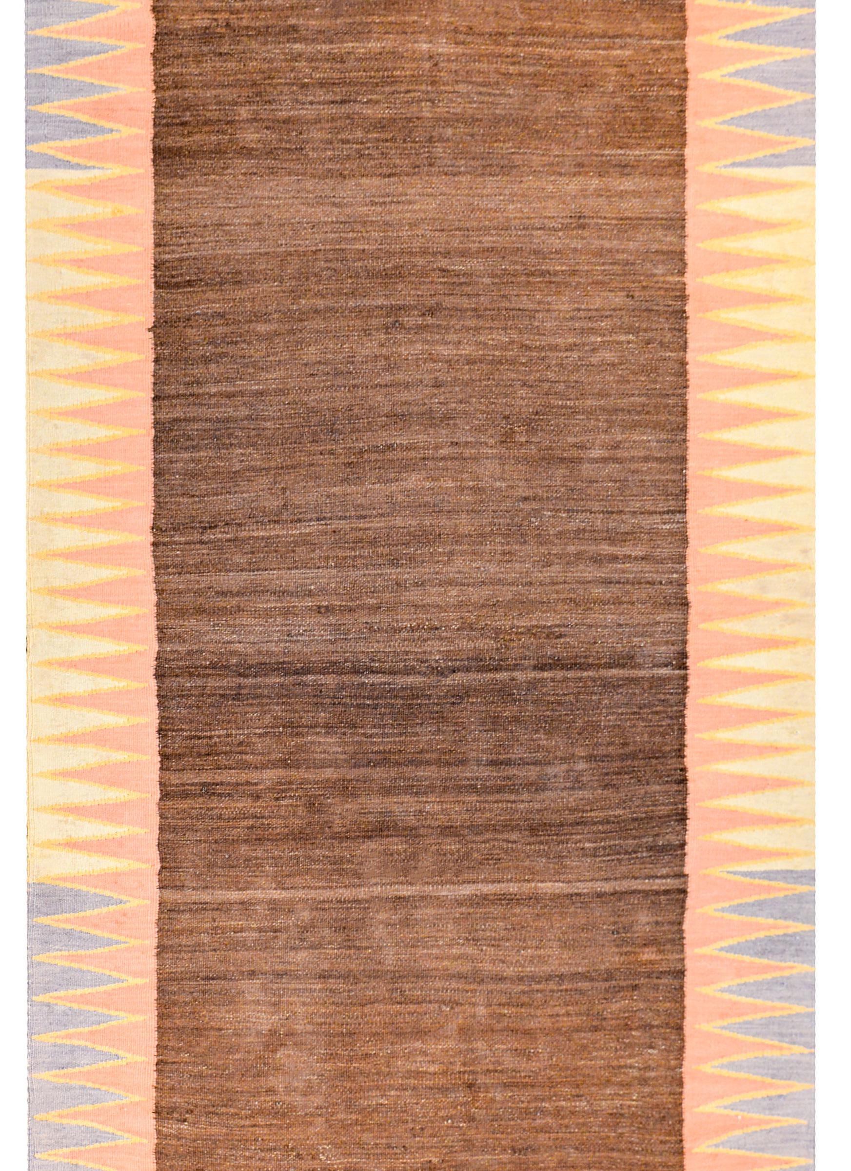 An early 20th century Persian Shahsevan kilim runner with a beautiful pattern containing a central field of natural, undyed, brown wool, surrounded by a pale indigo, gold, and crimson zigzag border running the length of the runner. Each end contains