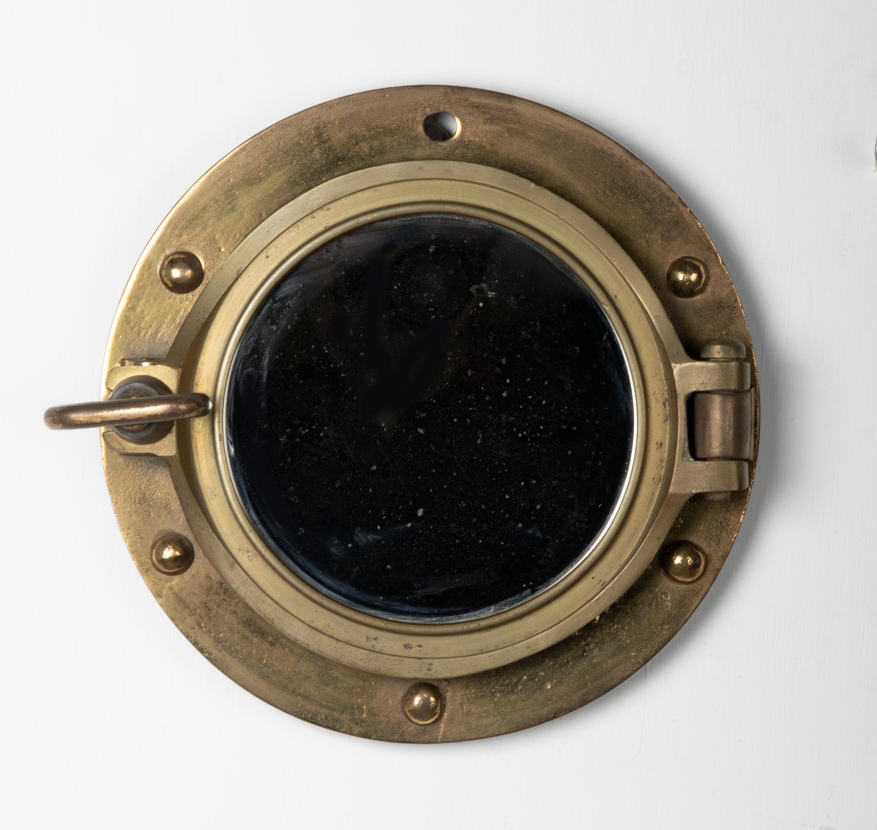 An antique ship porthole wall mirror made of brass. A mirror glass has been placed inside. The whole has a beautiful old patina. This maritime object was made around 1900-1930, origin unknown. The original bolt at the top is missing

The
