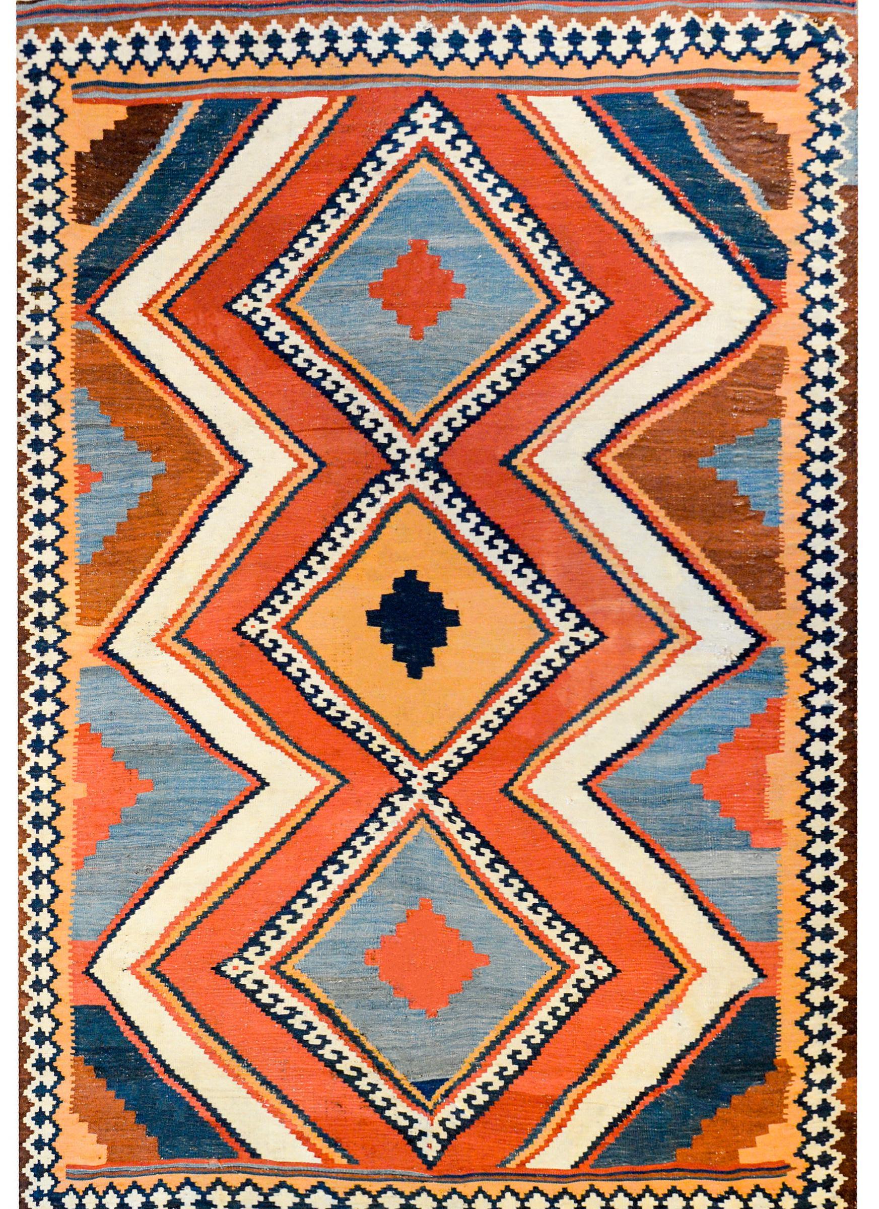 A wonderful early 20th century Persian Shiraz kilim rug with three large diamond medallions flanked by wide zigzags woven in indigo, orange, crimson, black, and white vegetable dyed wool surrounded by even more multicolored zigzag stripes.