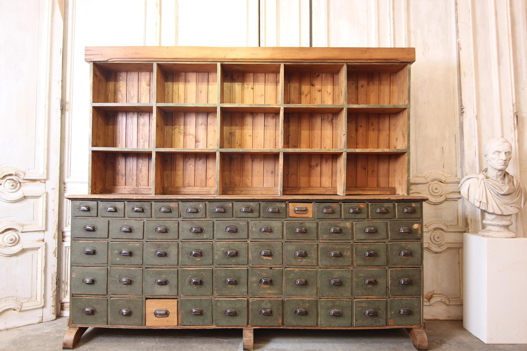 Original drawer cabinet from an early 20th century colonial goods shop. Solidly made of pine wood. 

2-part, consisting of a drawer cabinet with a total of 53 drawers and the shelf attachment.

Dimensions: 
97 cm/ 201 cm high, 235 cm wide, 46
