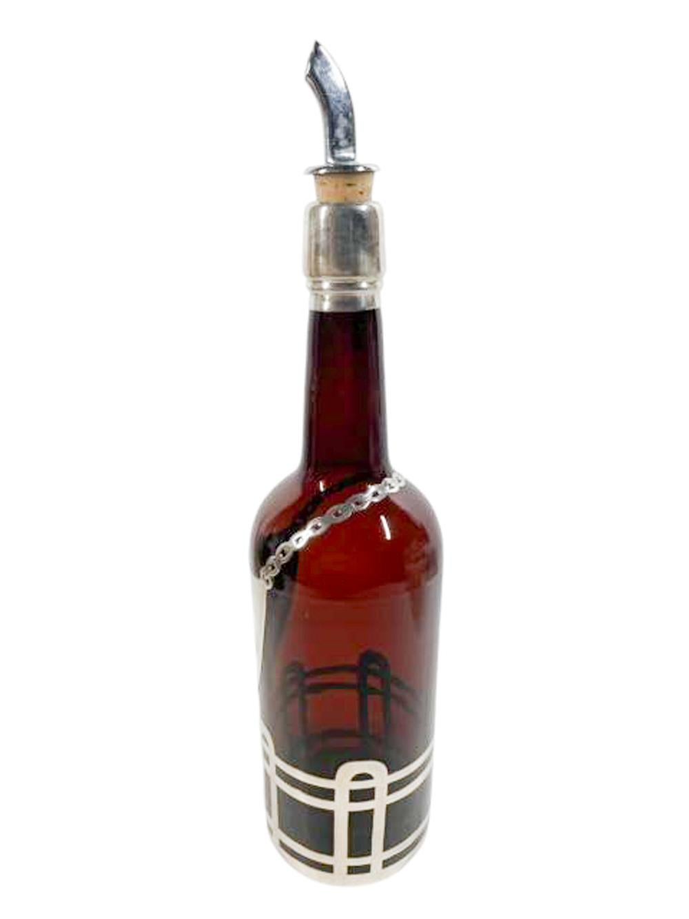Early 20th century dark amber glass back bar bottle with sterling silver overlay decoration. Decorated with a silver shield-form decanter label (monogrammed) with a chain around the shoulder and above a geometric design at the base as well as the