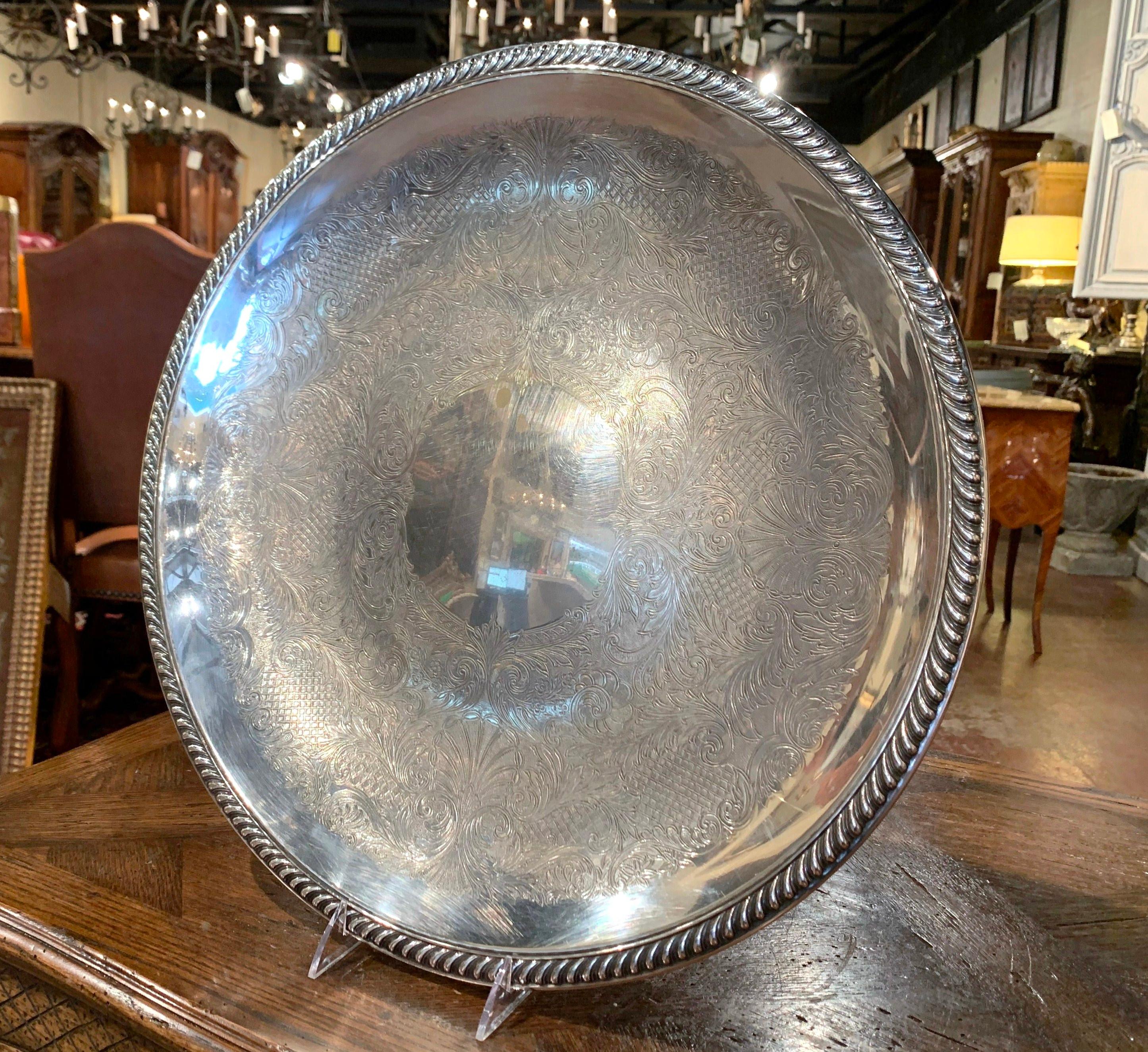 Created in France circa 1920, and round in shape, the large brass tray with silver plate features engraved floral and shell decor with a repousse motif around the rim. The decorative tray is in excellent condition commensurate with age and use with